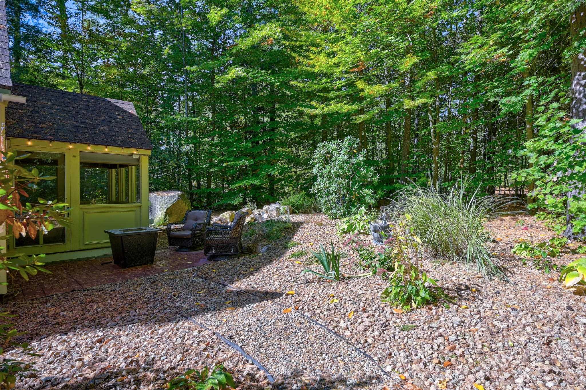 Wooded patio with a green sunroom, outdoor chairs, and a landscaped gravel garden.