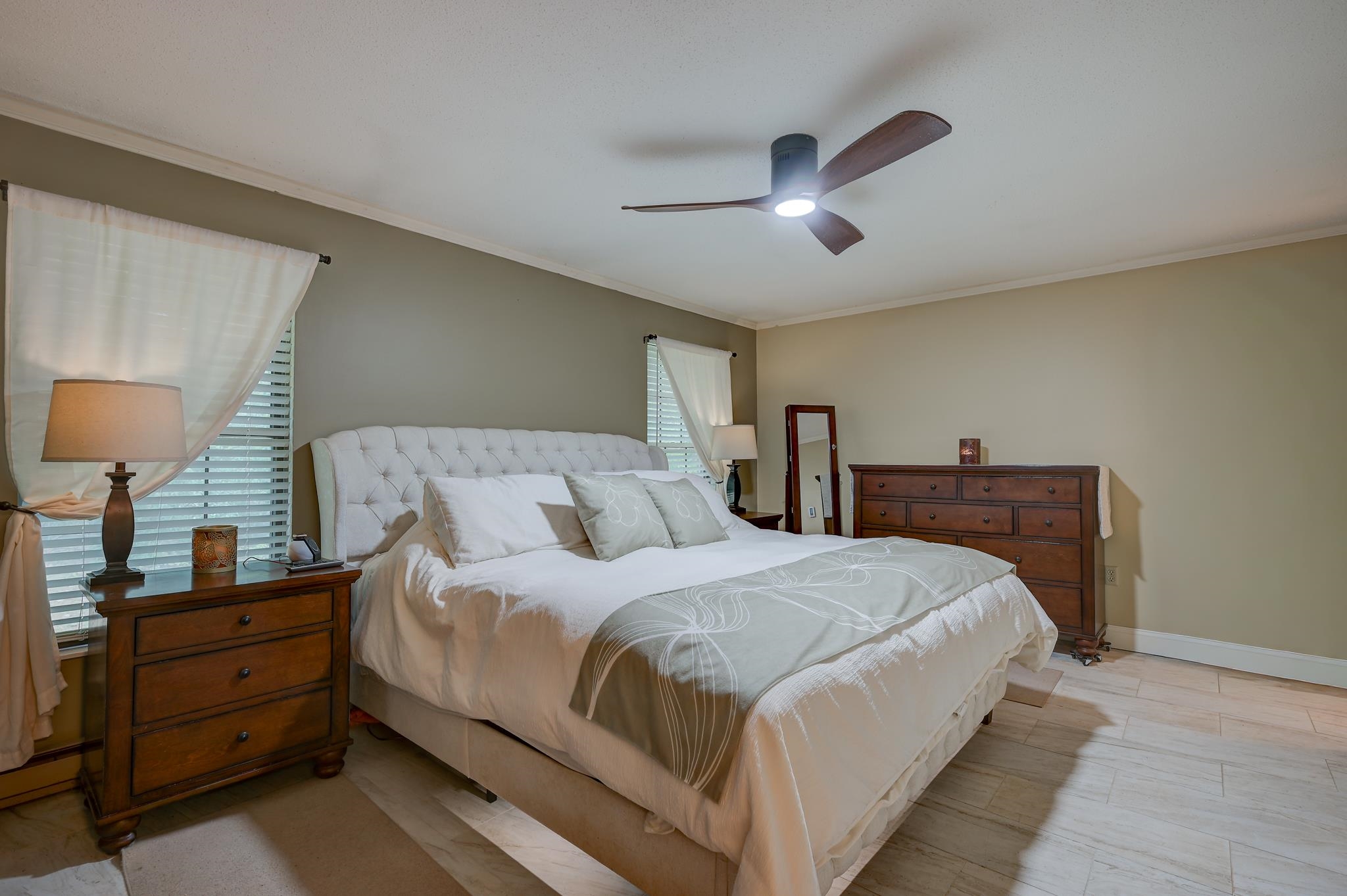 Furnished bedroom with a tufted white bed, wooden dresser, and ceiling fan.