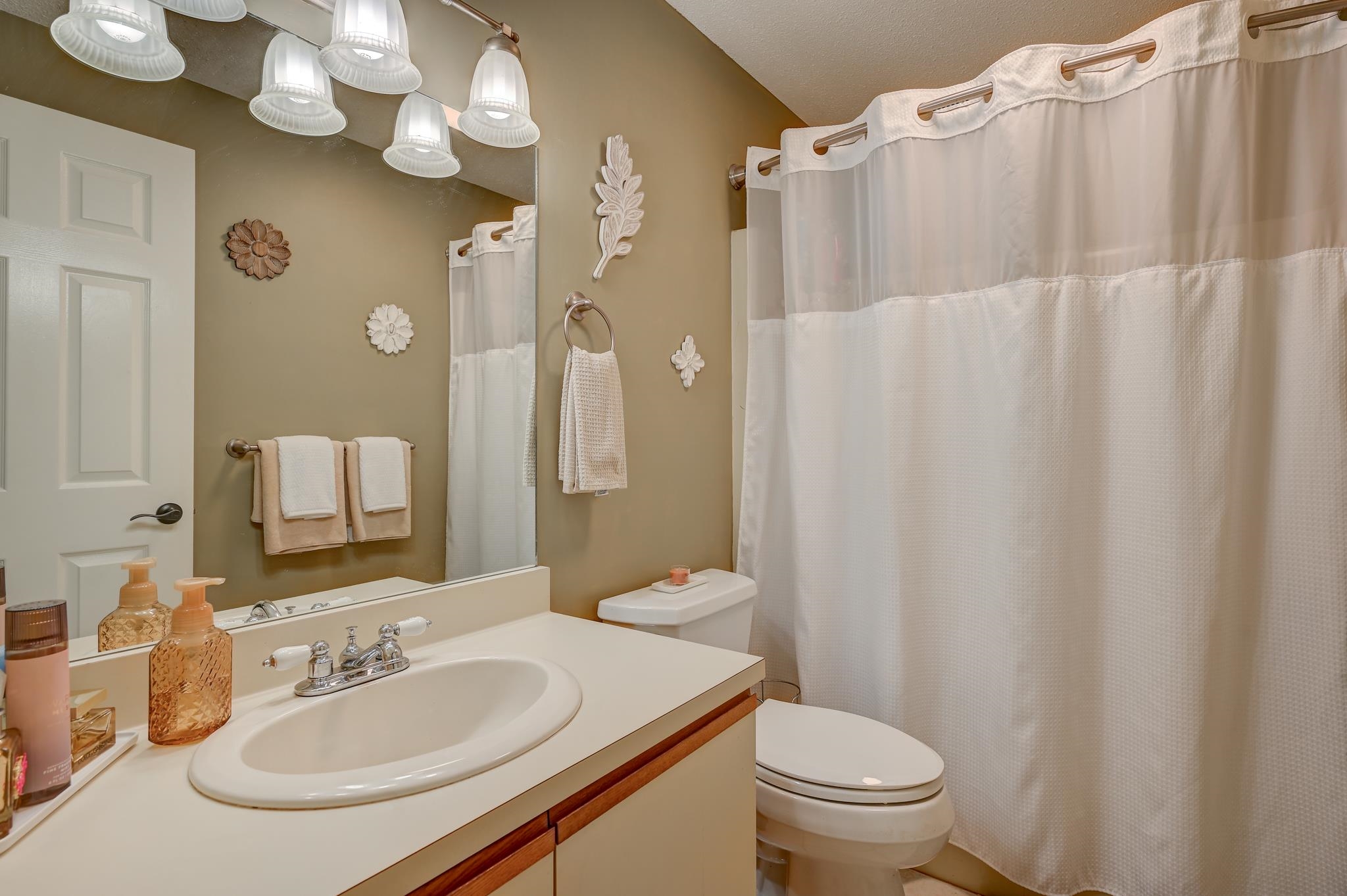 Bathroom with a white vanity, oval sink, large mirror, and white shower curtain.