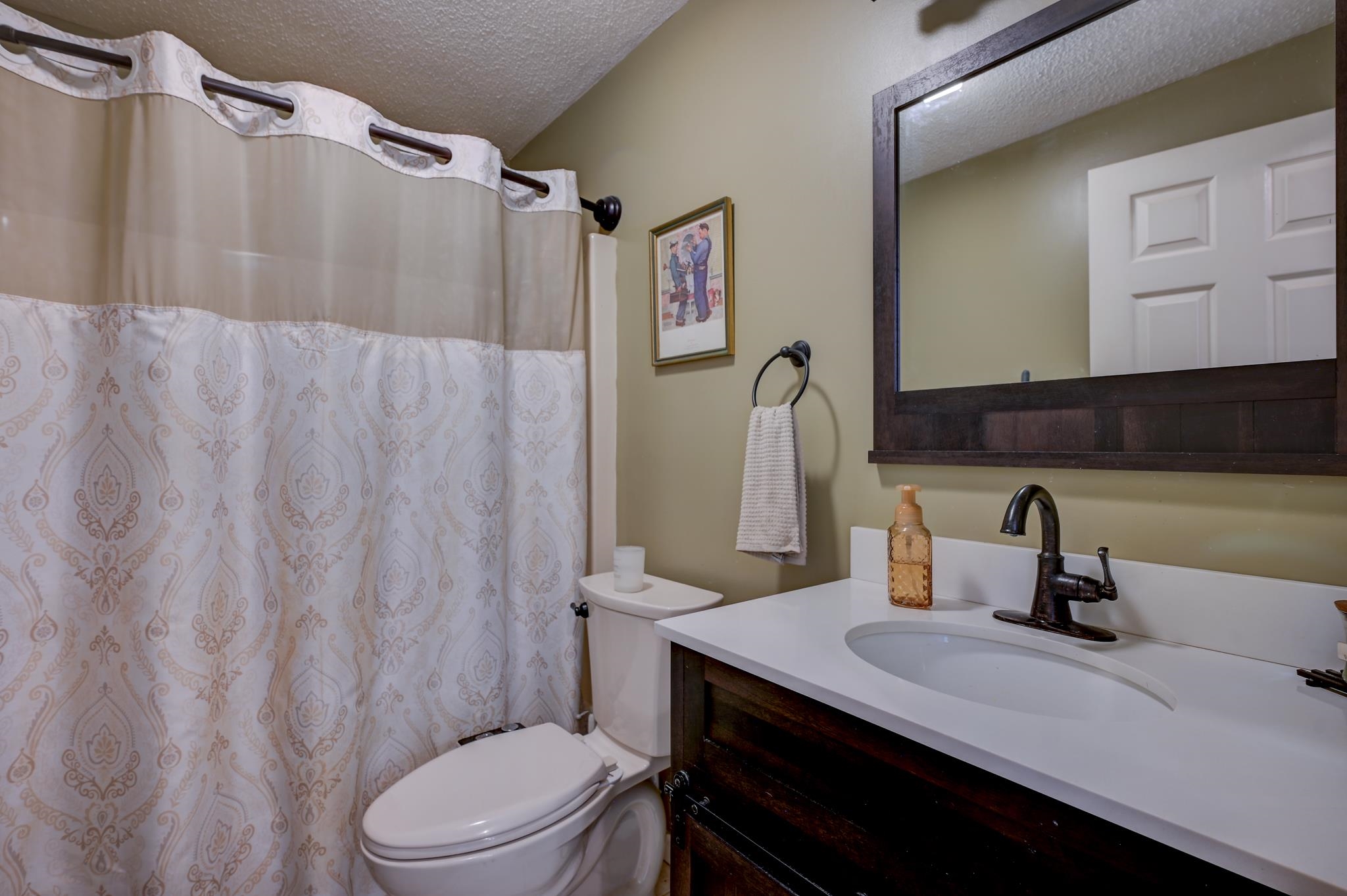 Bathroom with a patterned shower curtain, white sink, and dark wood vanity.