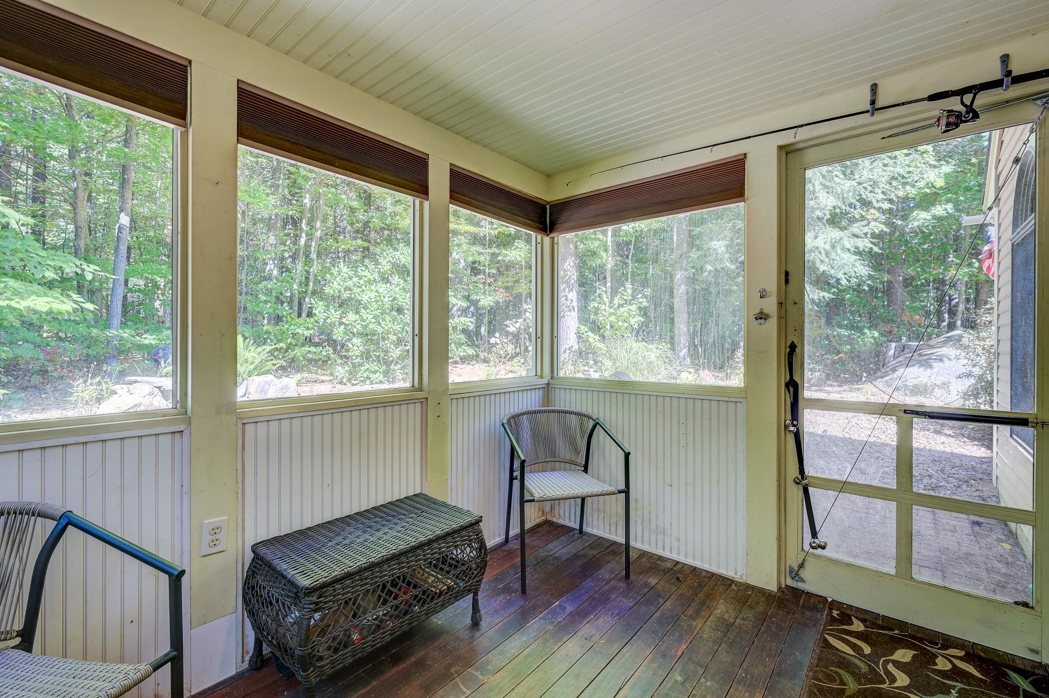 Enclosed porch with wicker seating, broad windows, and a view of the surrounding woods.