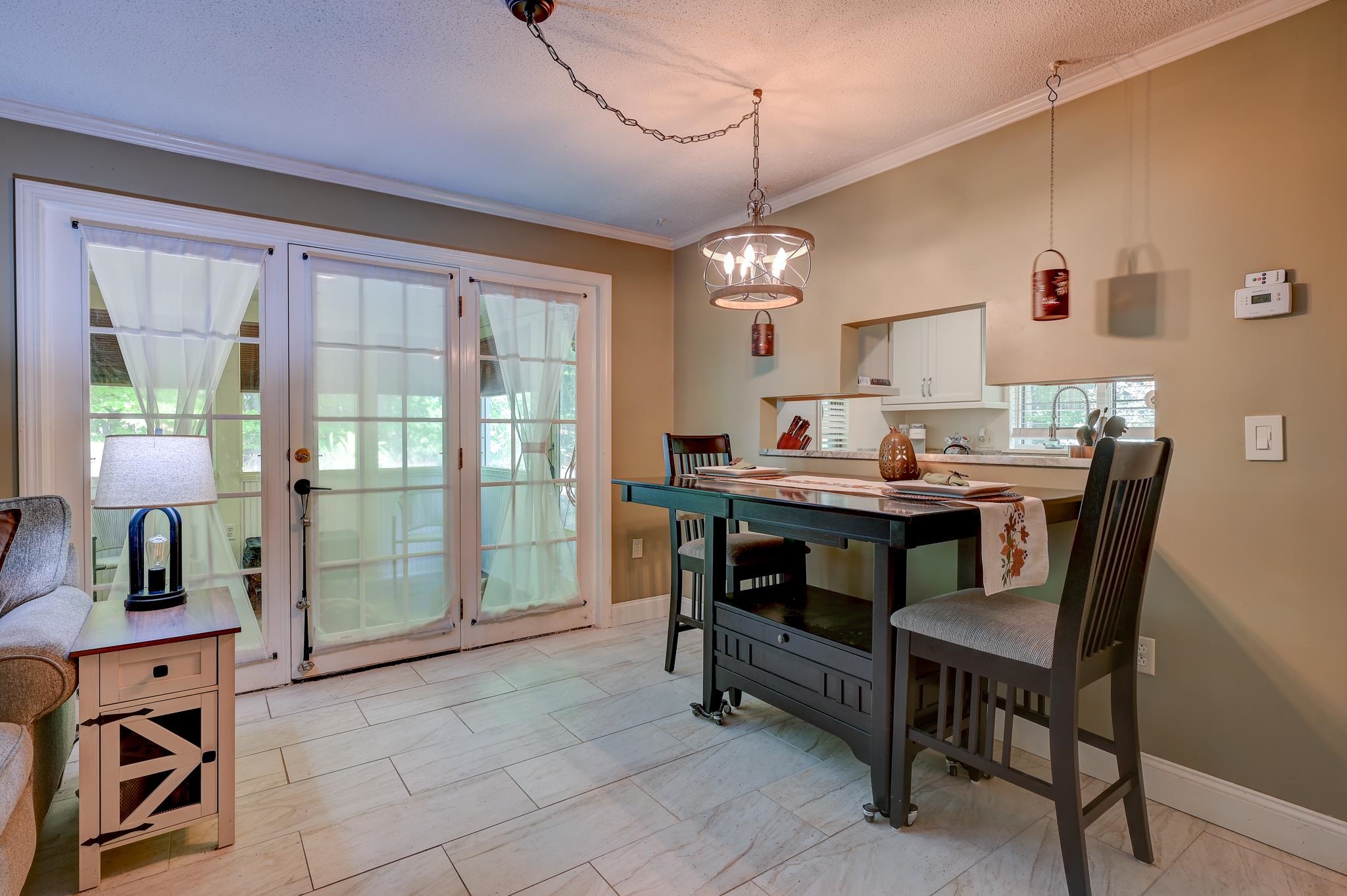 Dining area with a dark table beside curtained glass doors and an adjoining kitchen.