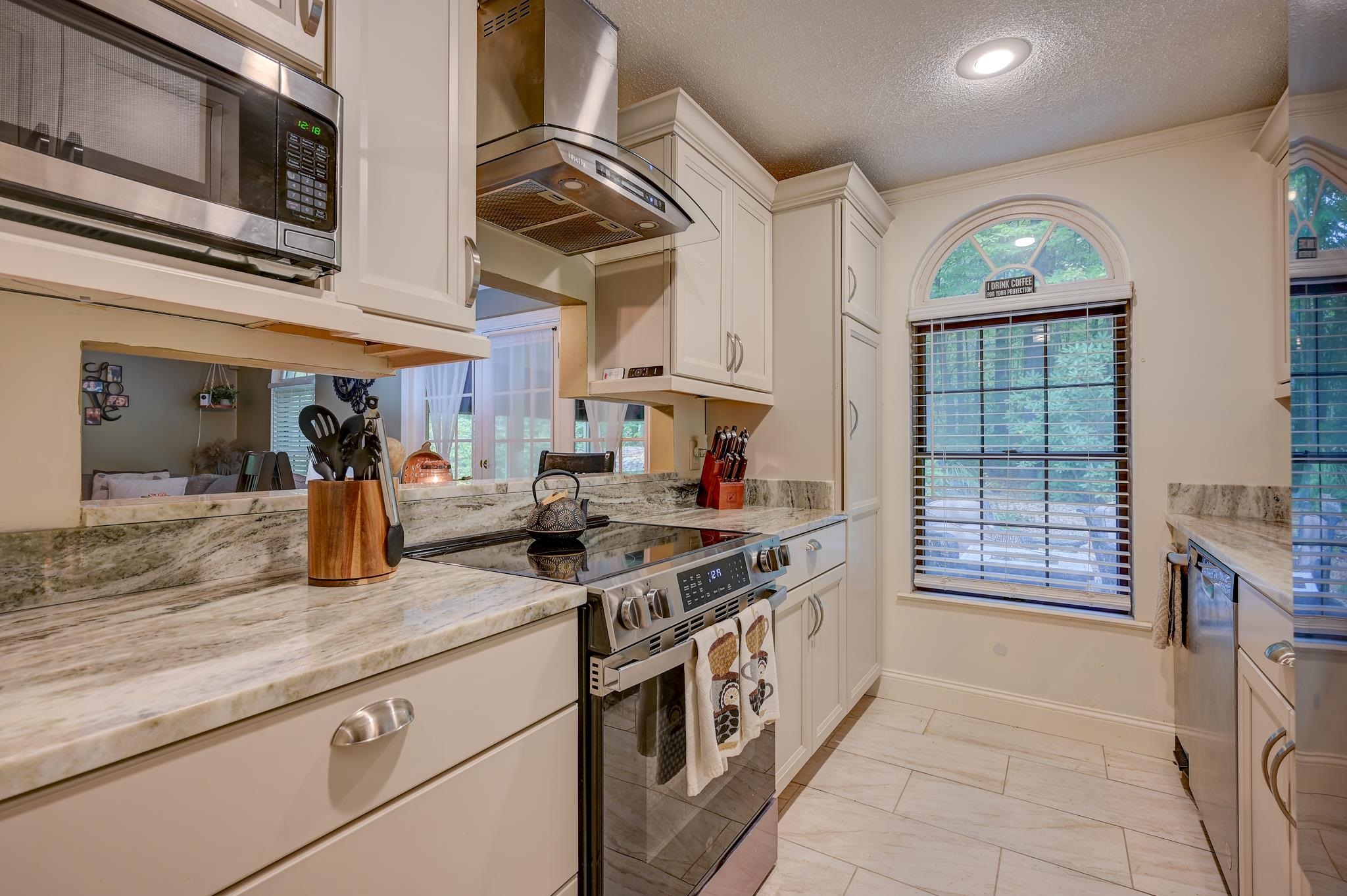 Kitchen with white cabinets, granite counters, stainless steel appliances, and an arched window.