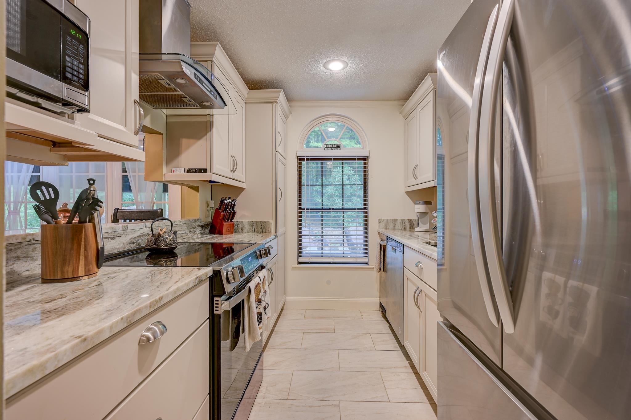 Galley kitchen with white cabinets, granite counters, stainless steel appliances, and an arched window.