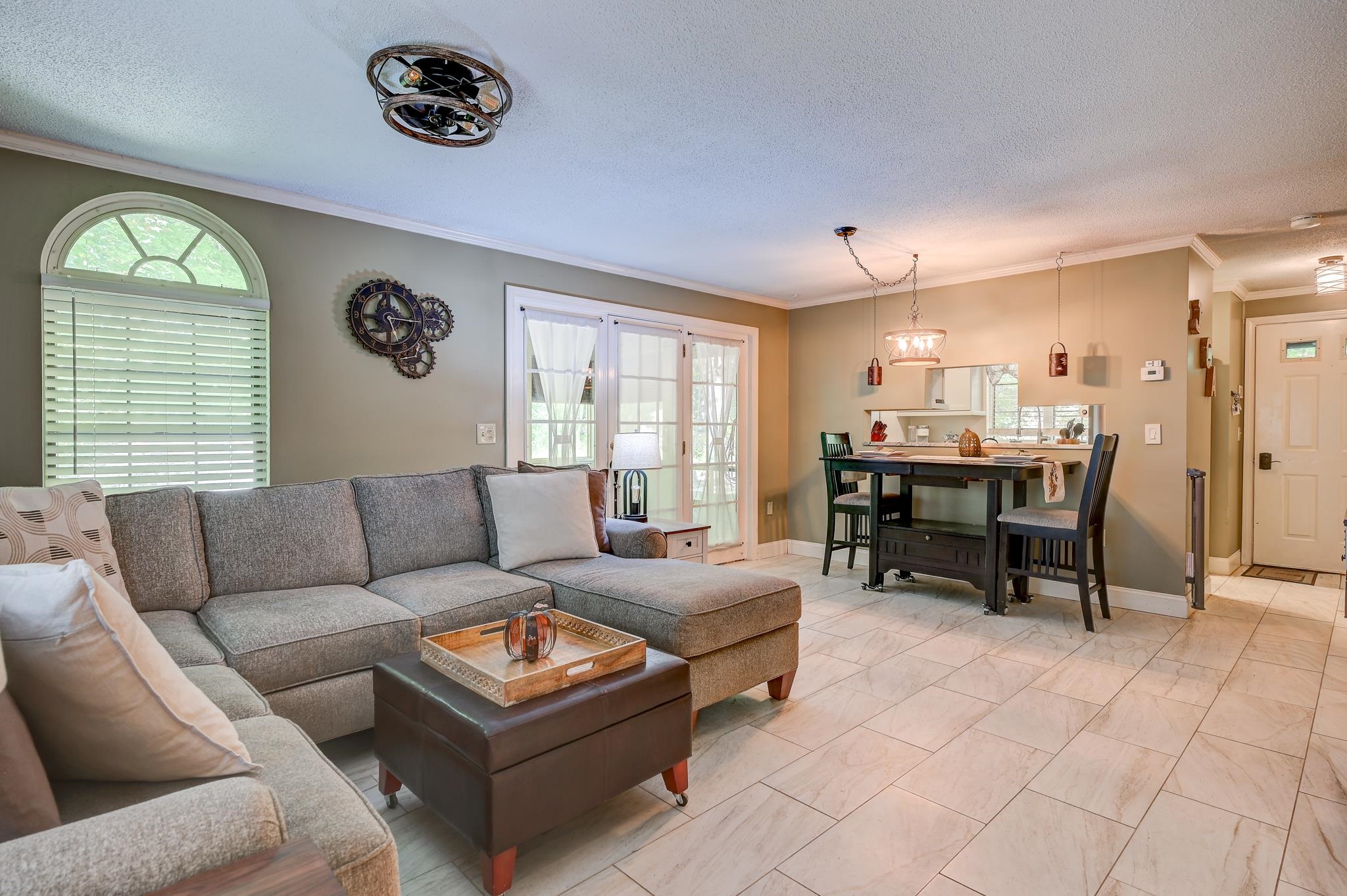 Living and dining room with a gray sectional, arched window, glass doors, and tiled floor.