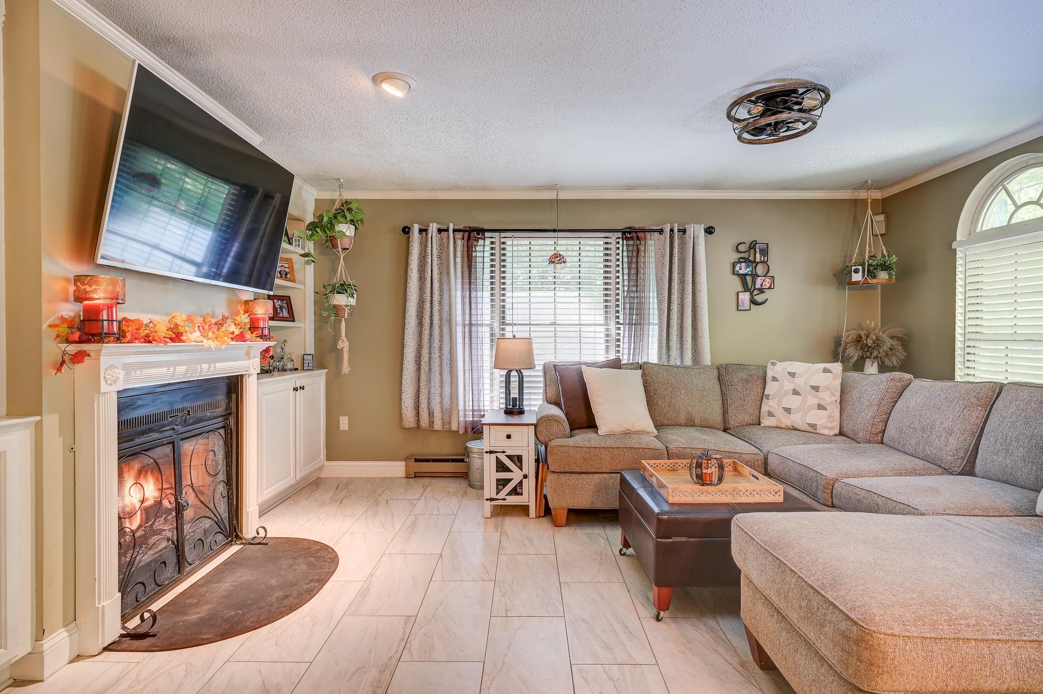 Living room with a gray sectional, decorated fireplace, wall-mounted television, and arched window.