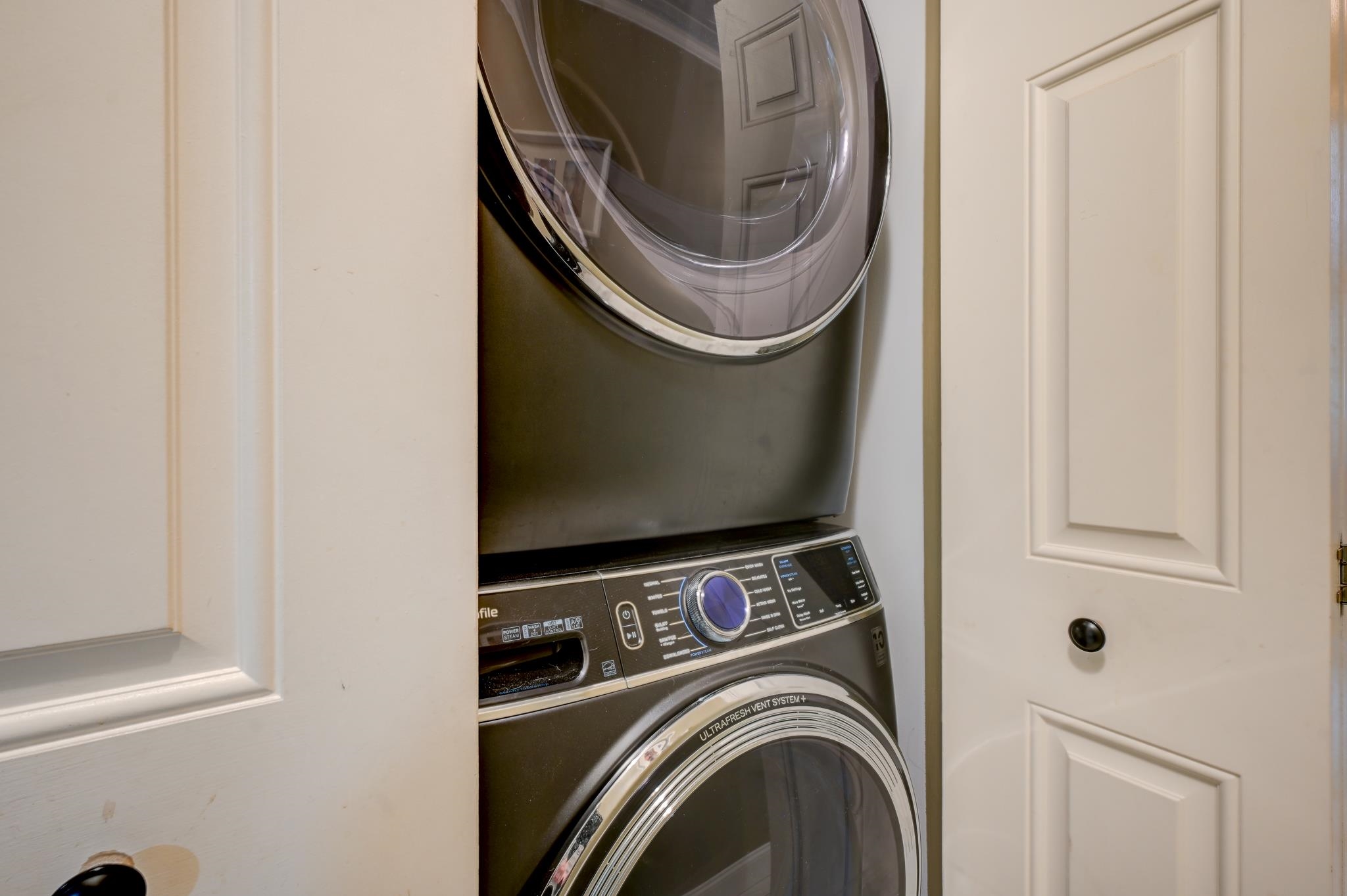 Stacked dark washer and dryer in a narrow closet between white paneled doors.