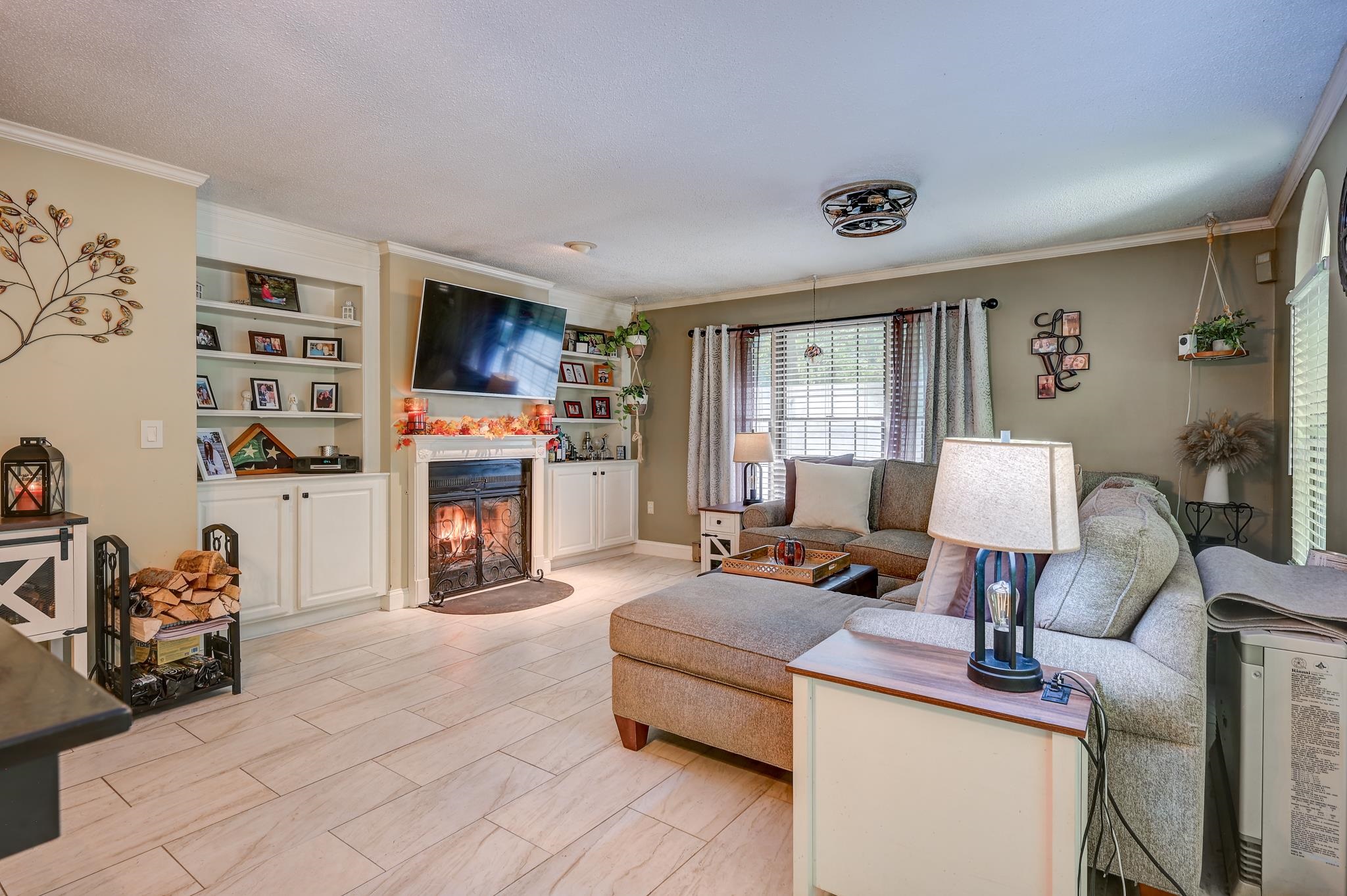 Living room with a gray sectional, tiled floors, built-in shelves, and a lit fireplace.