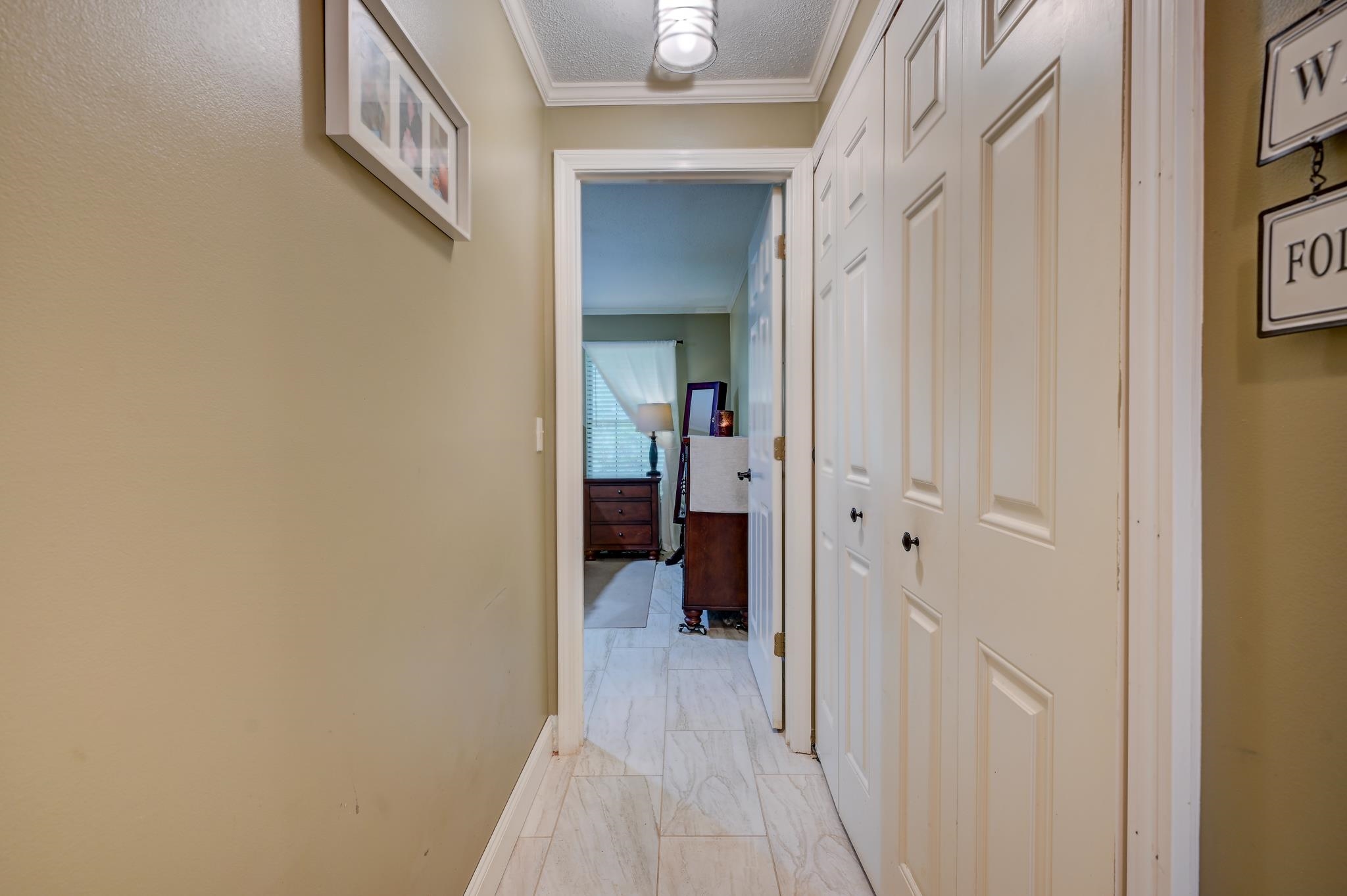 Hallway with white paneled doors and marble-look tile, looking into a furnished room.