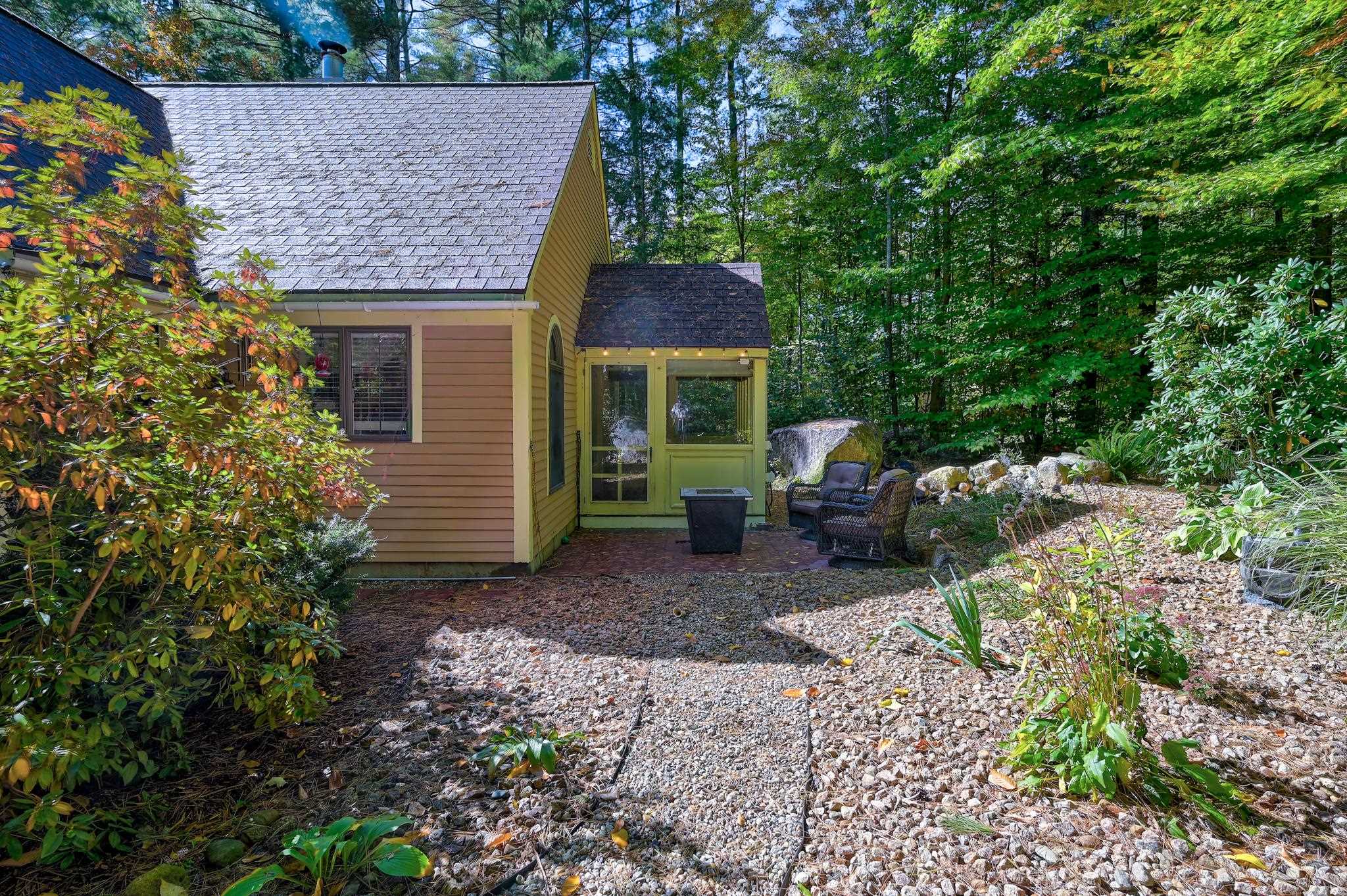 Woodland home with a green sunroom, gravel patio, and outdoor seating.