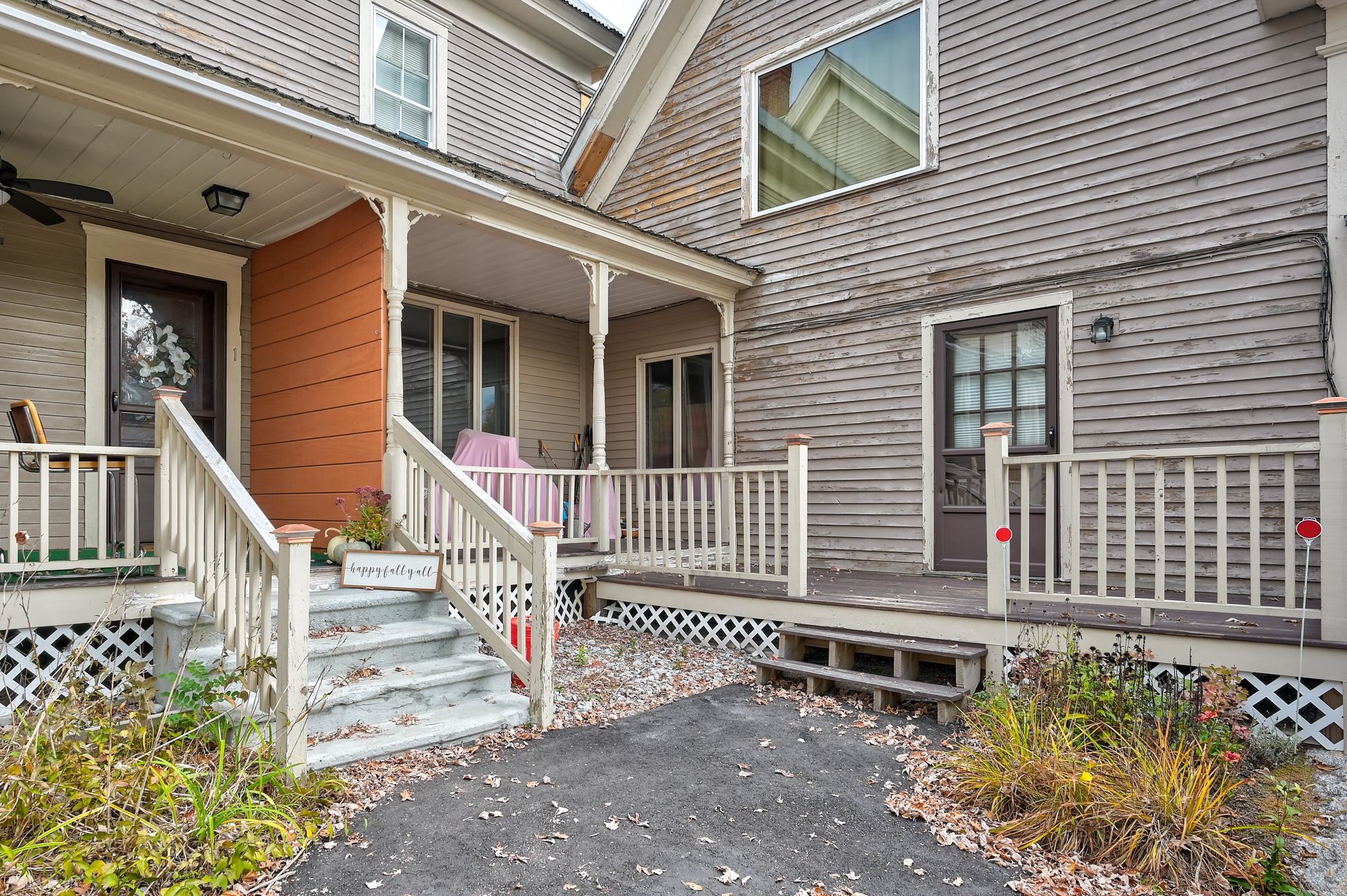 Home entrance with a covered porch, white railings, and a raised deck surrounded by fall leaves.