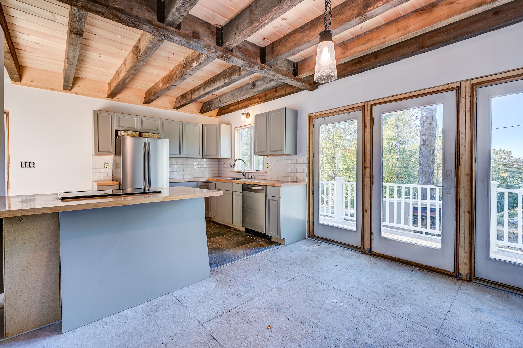 Kitchen with an island cooktop, exposed timber ceiling beams, and glass doors opening to a deck.
