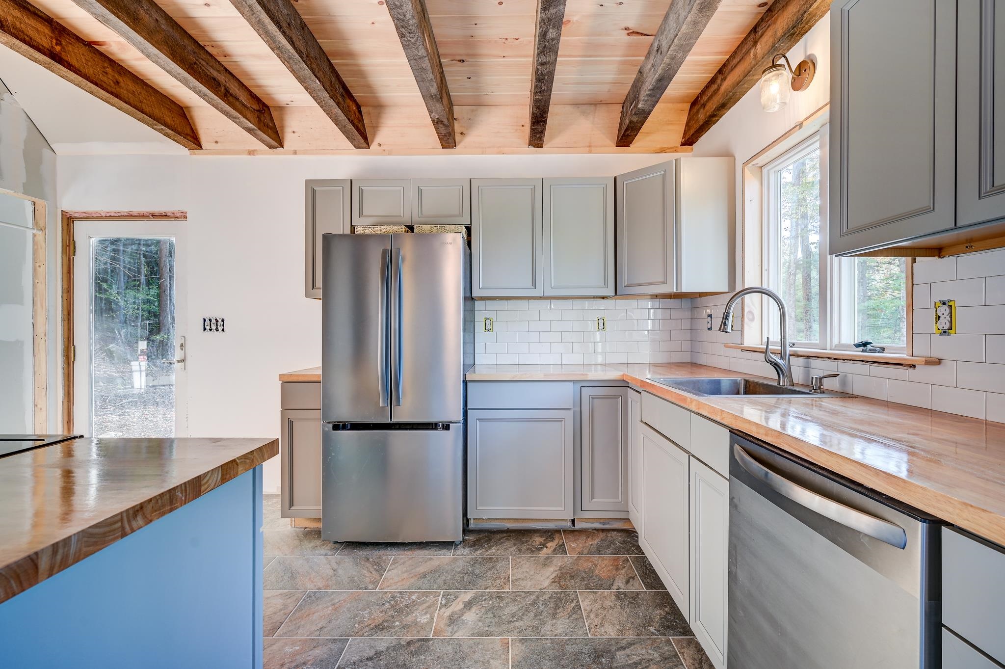 Kitchen with exposed wood ceiling beams, gray cabinets, and stainless steel appliances.
