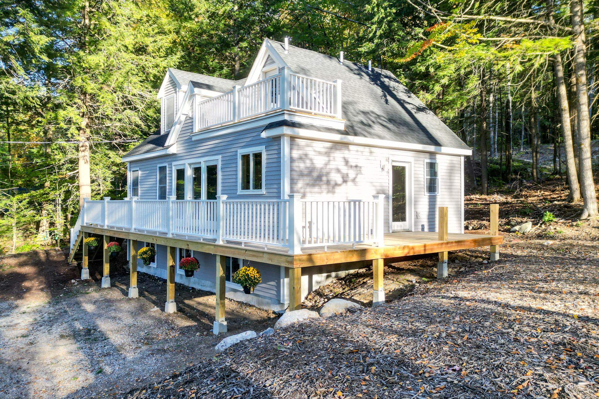 Blue-gray house among trees with a raised deck, white railings, and an upper balcony.