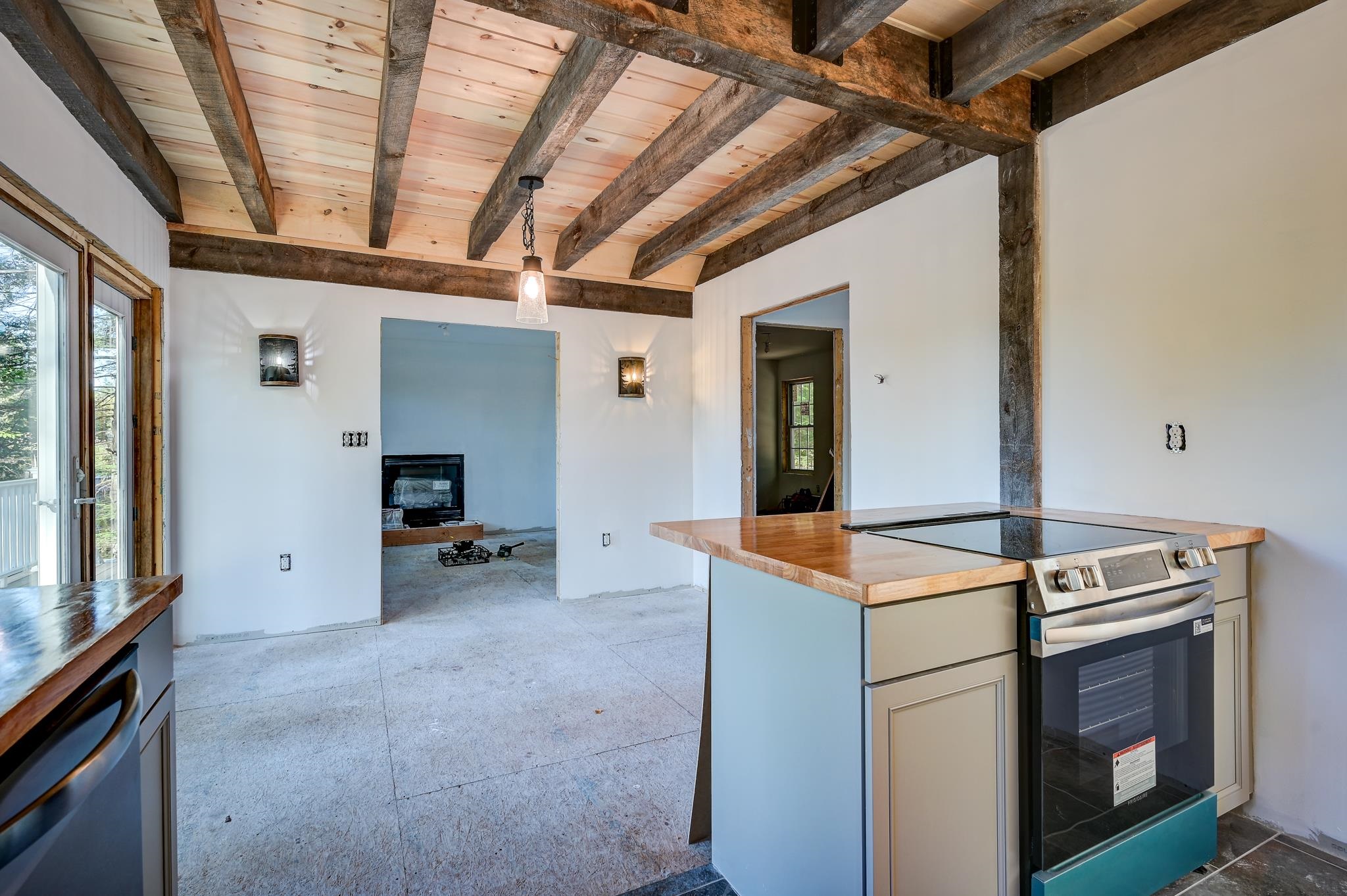 Kitchen with exposed timber beams, a wood-topped island and cooktop, and an adjoining fireplace.