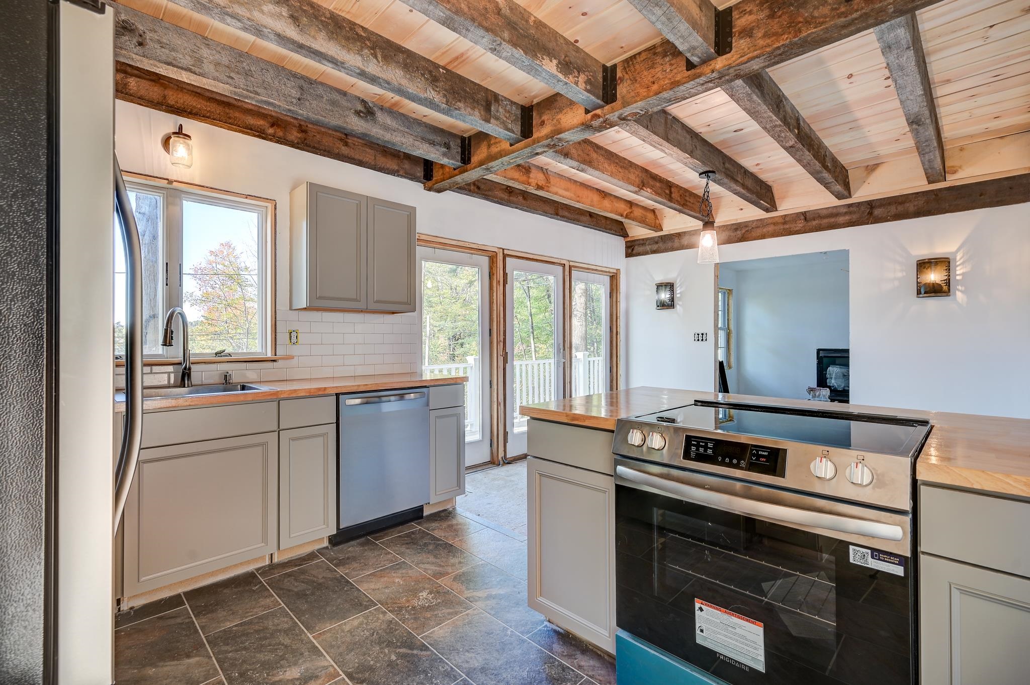 Kitchen with exposed timber ceiling beams, gray cabinets, wood counters, and a stainless steel range.