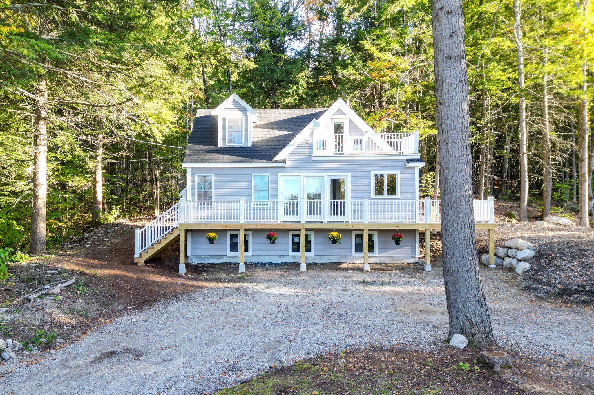 Light blue house with a broad white-railed deck and upper balcony, surrounded by trees.