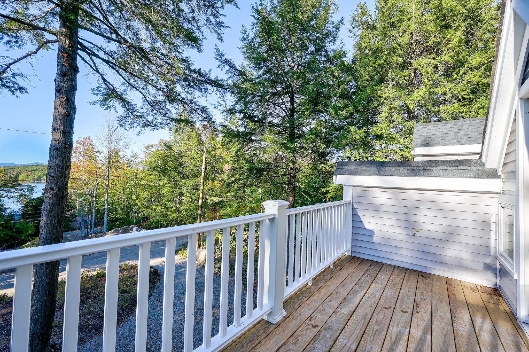 Wooden deck with white railings overlooking a tree-lined lake and distant hills.