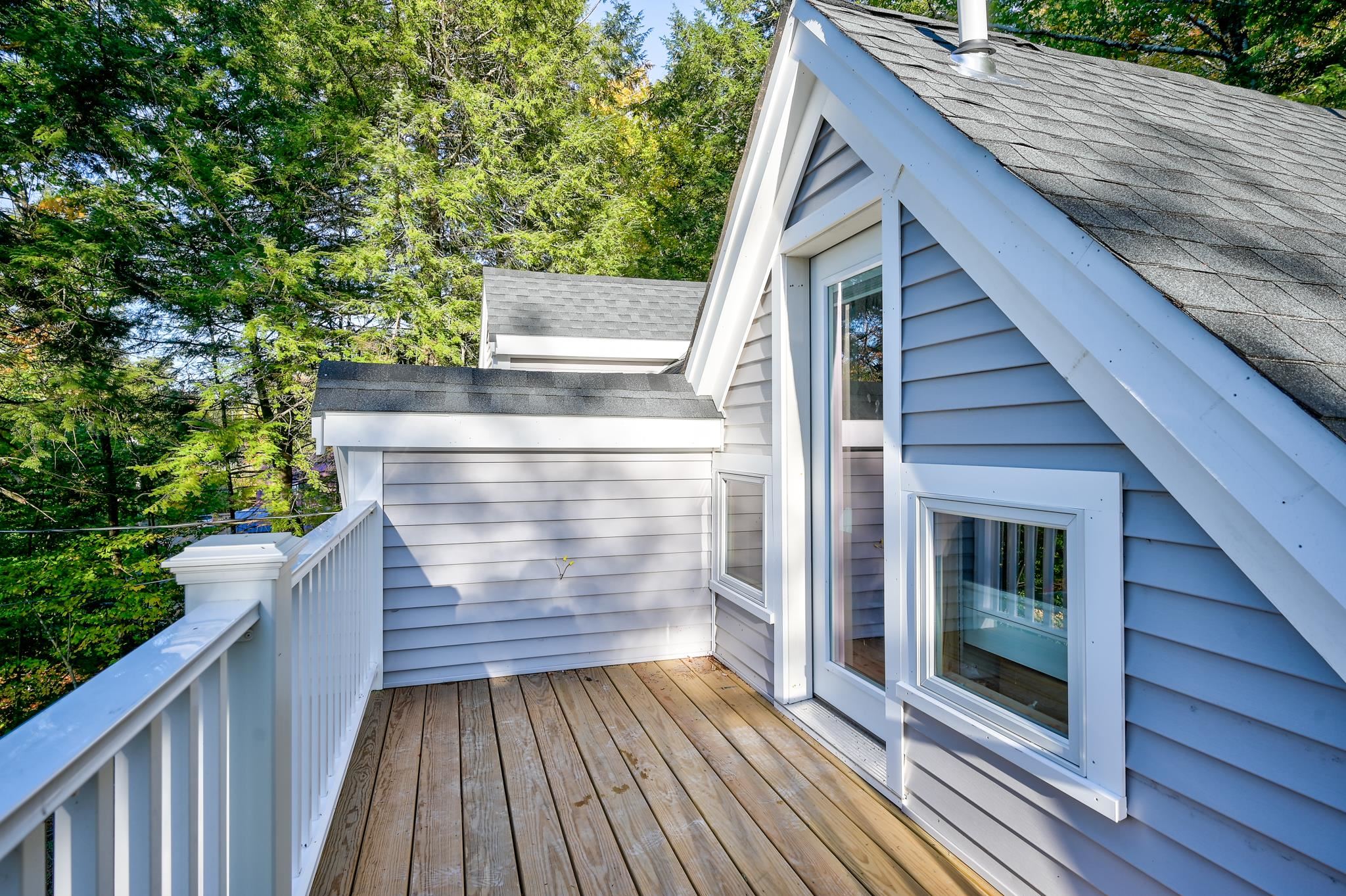 Wooden deck beside a blue-gray home, with white railings and a wooded setting.