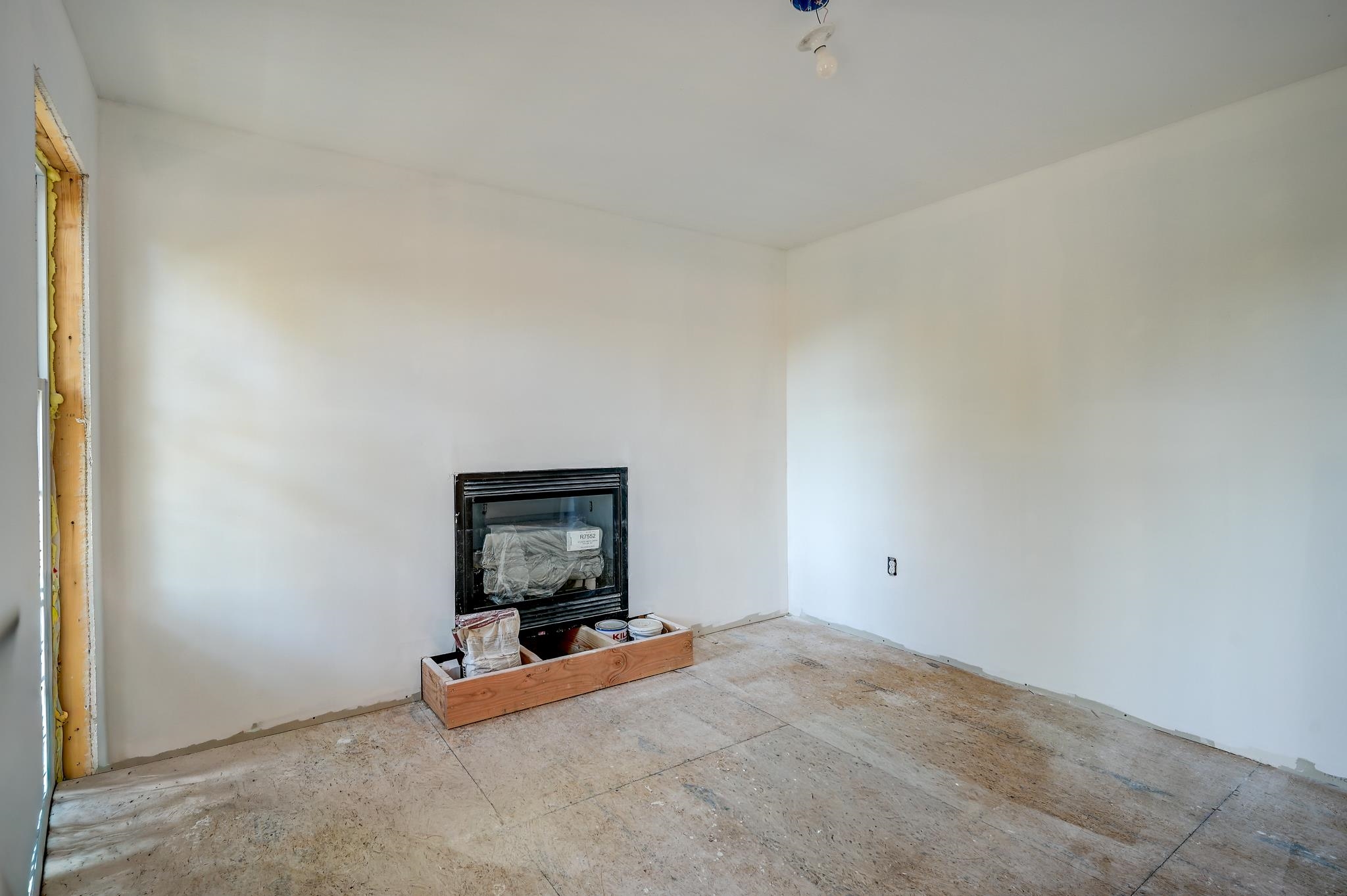 Unfinished room with a black fireplace insert, exposed subfloor, and paint supplies.