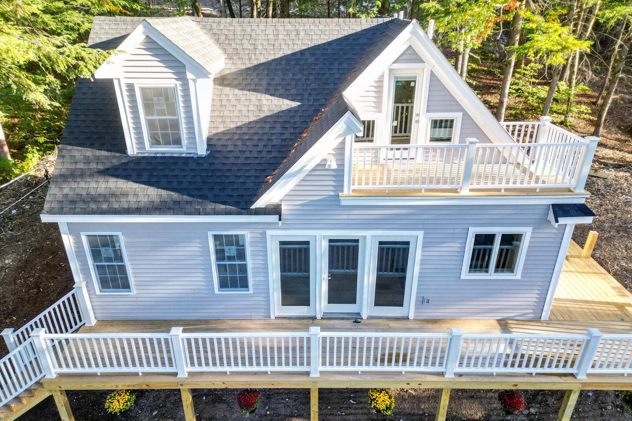 Rear of a gray house with a large raised deck, white railings, and an upper-level balcony.