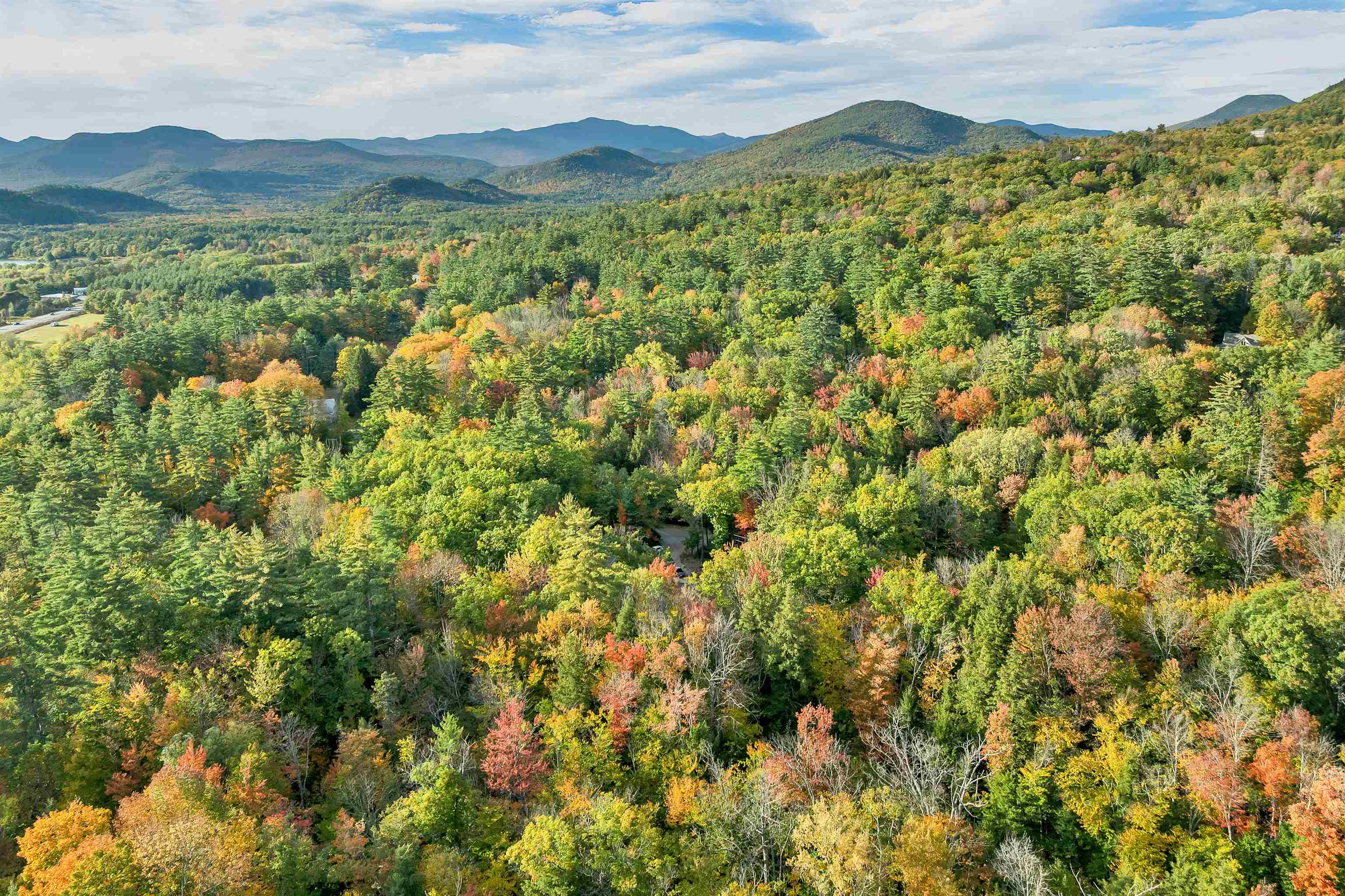 Aerial view of autumn forest and scattered homes, with mountain ridges in the distance.