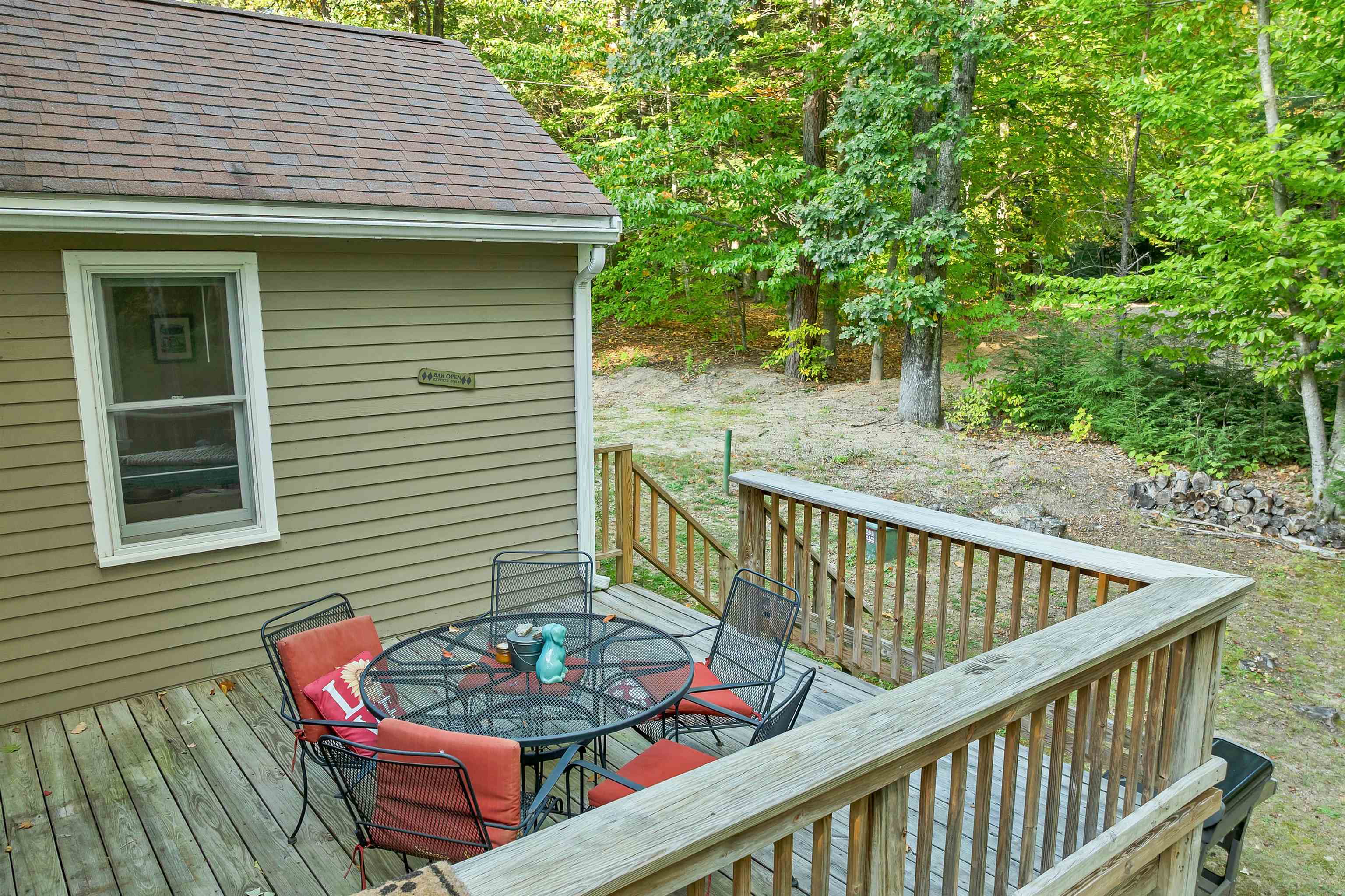 Furnished wooden deck with a round dining table and wooded yard beyond the railing.