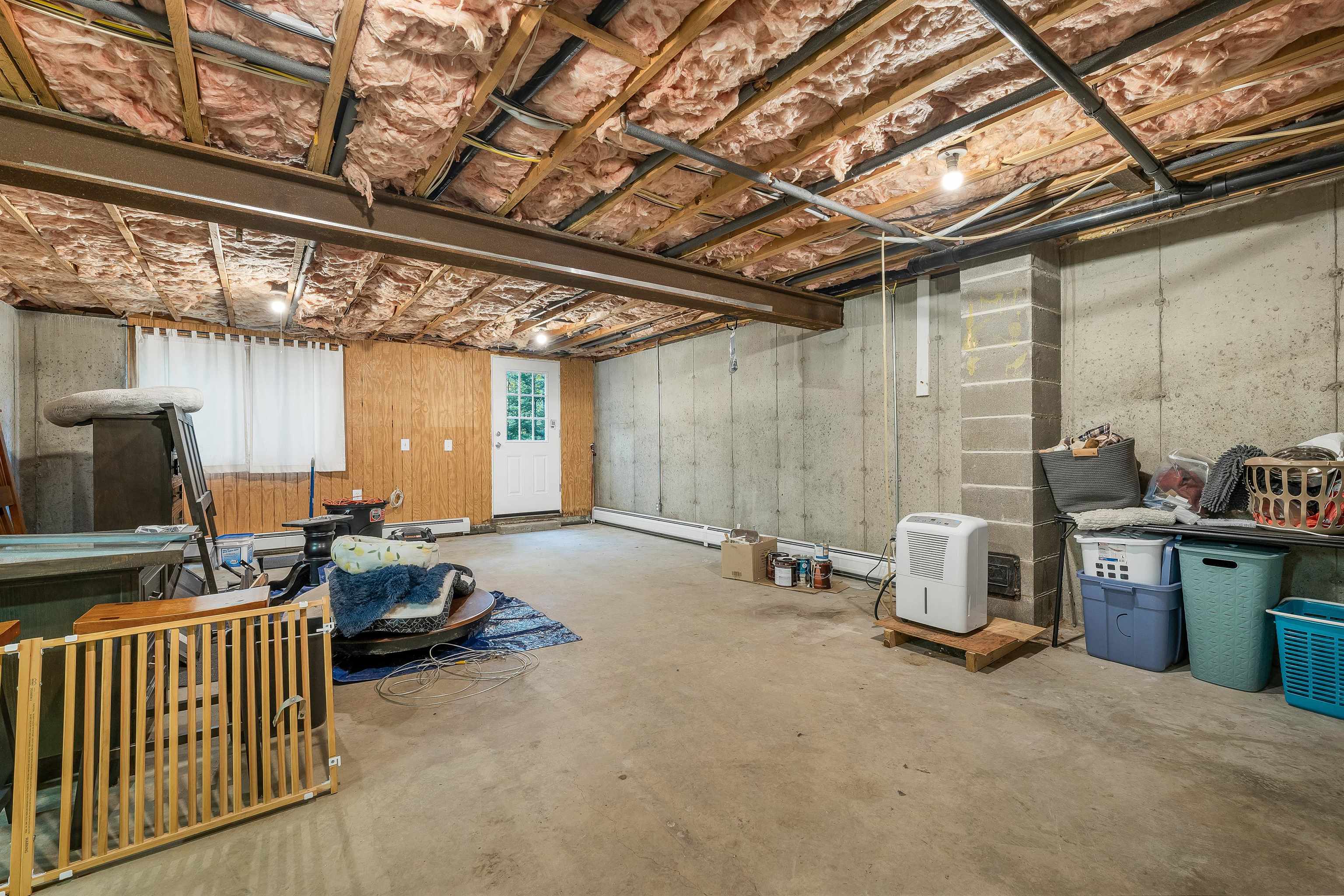 Unfinished basement with exposed ceiling insulation, concrete walls, and storage items.