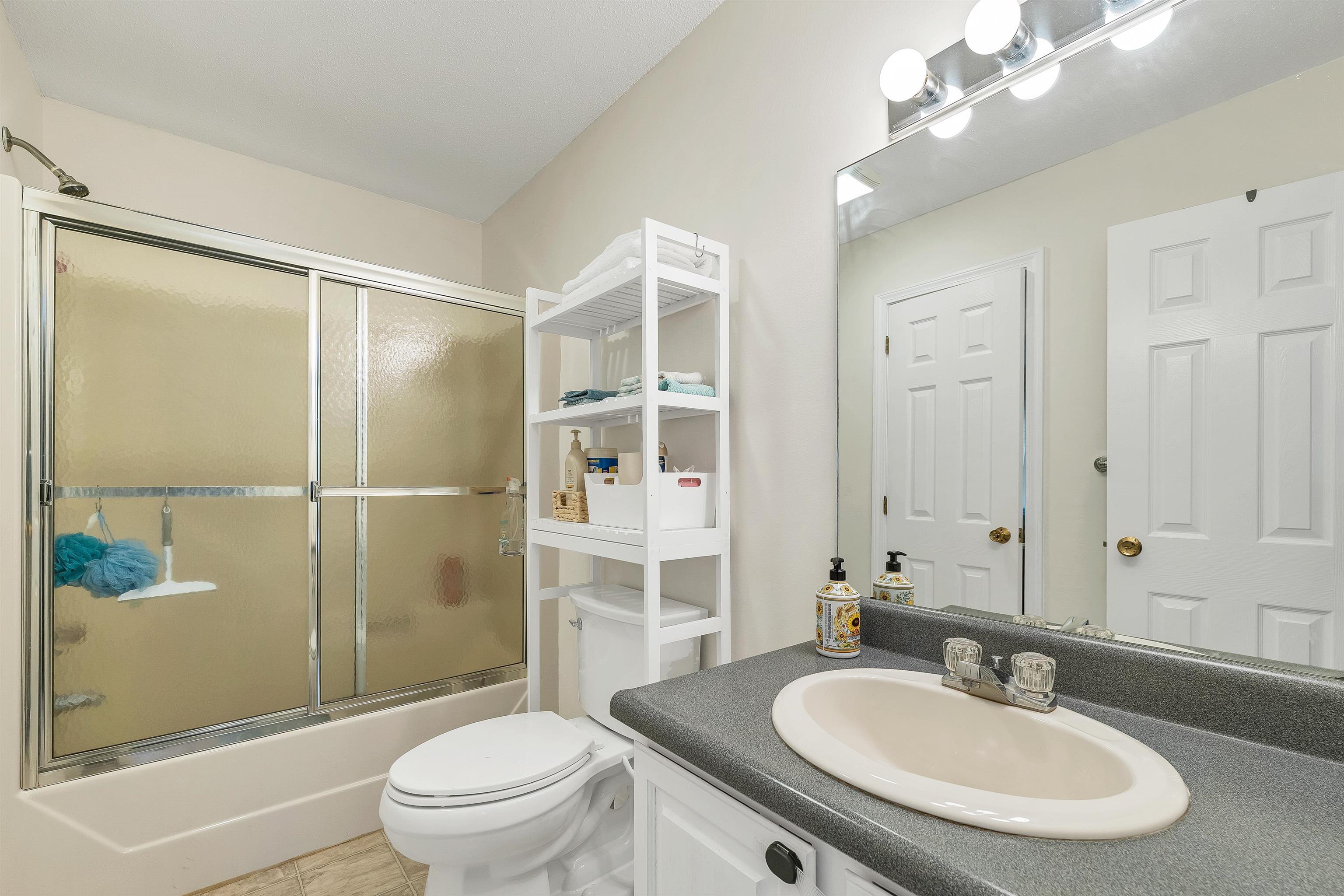 Bathroom with a frosted-glass tub and shower, toilet, and white vanity with dark countertop.