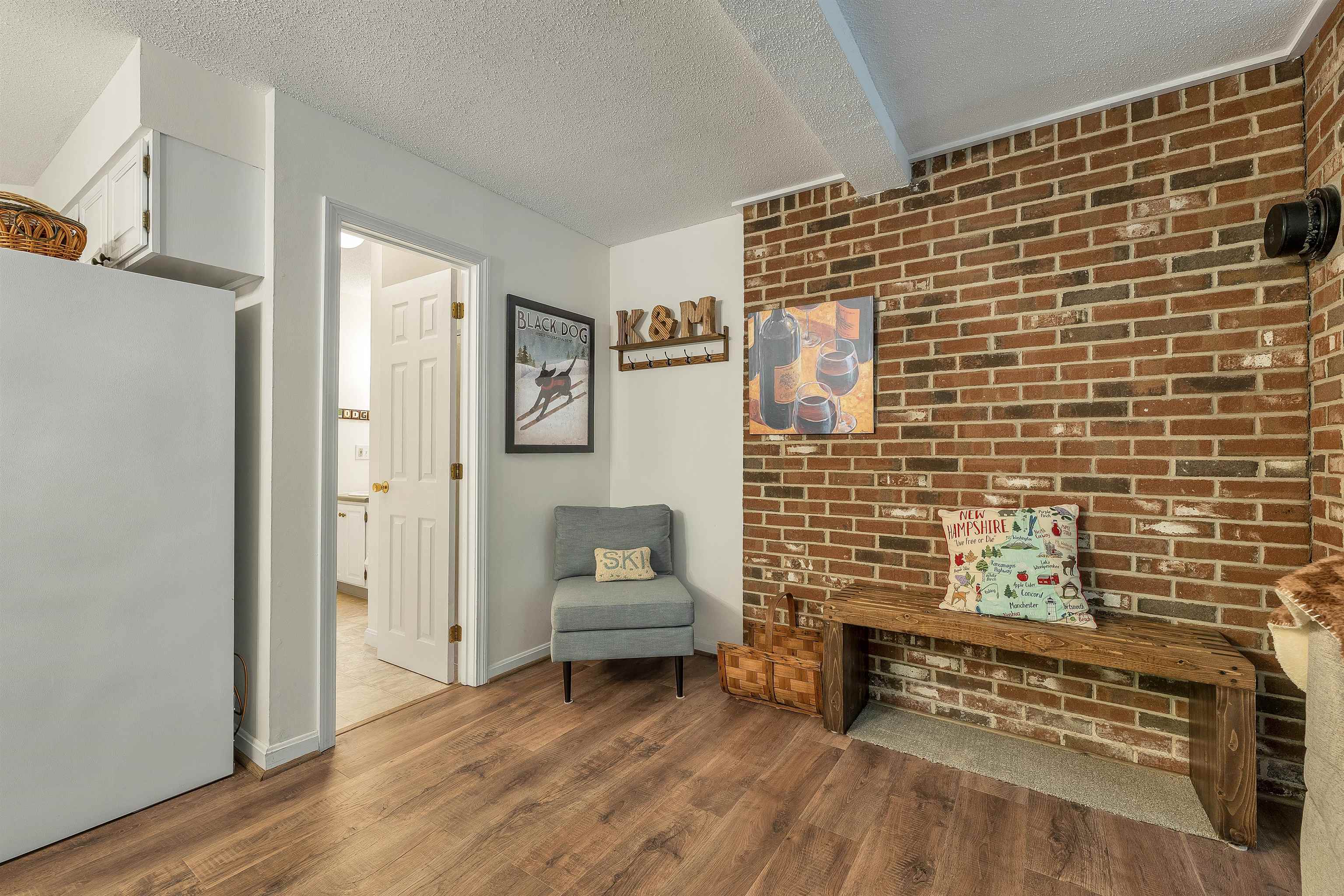 Entryway with a brick accent wall, rustic bench, gray chair, and doorway to an adjoining room.