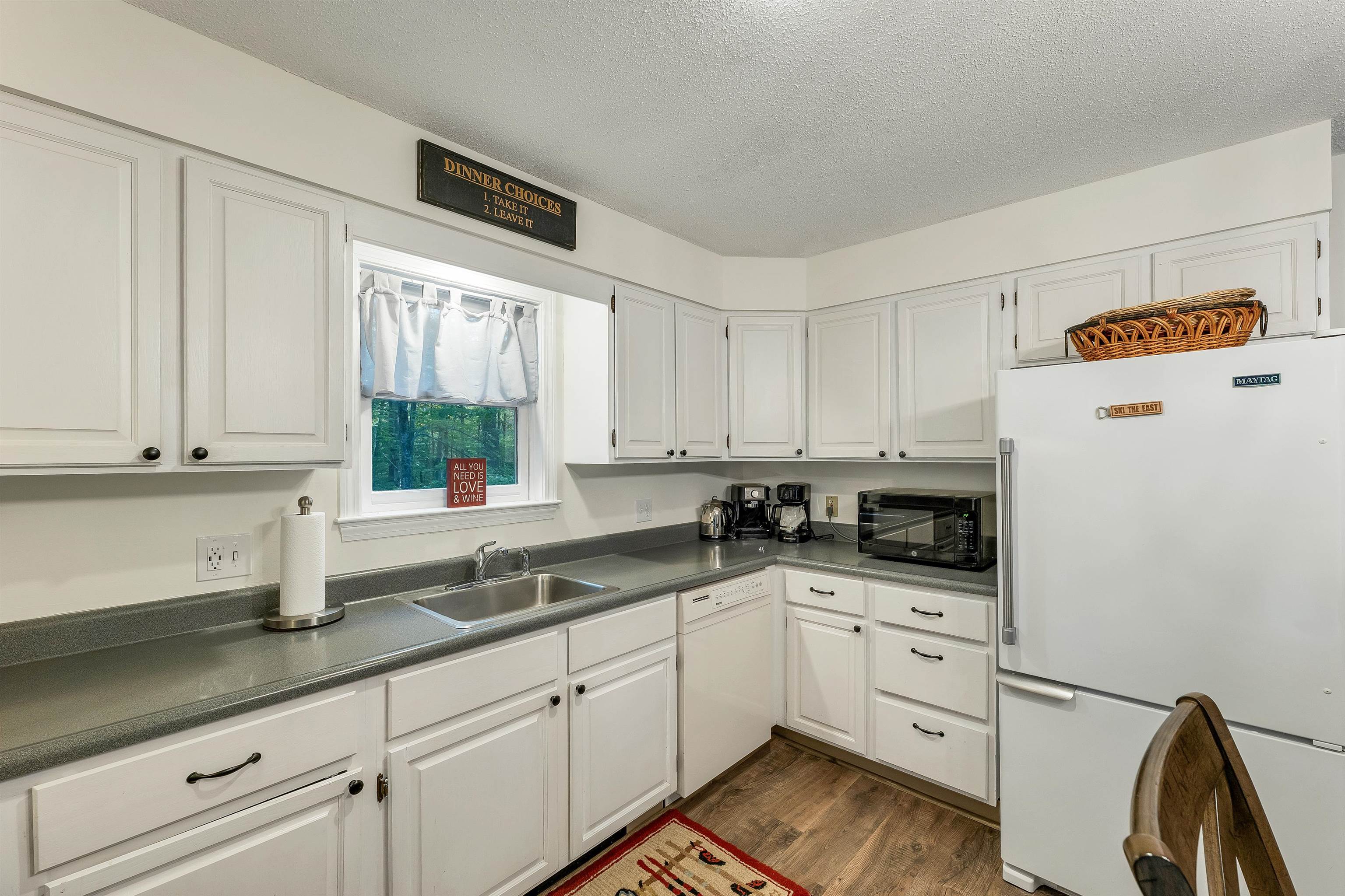Kitchen with white cabinets, gray countertops, and a window overlooking trees.