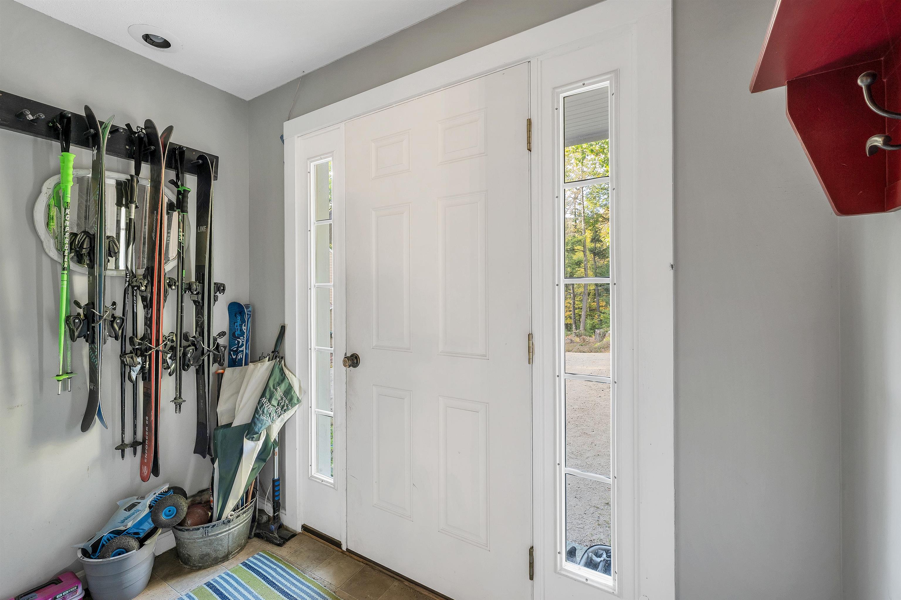 Entryway with skis and snowboards on a wall rack beside a white front door.
