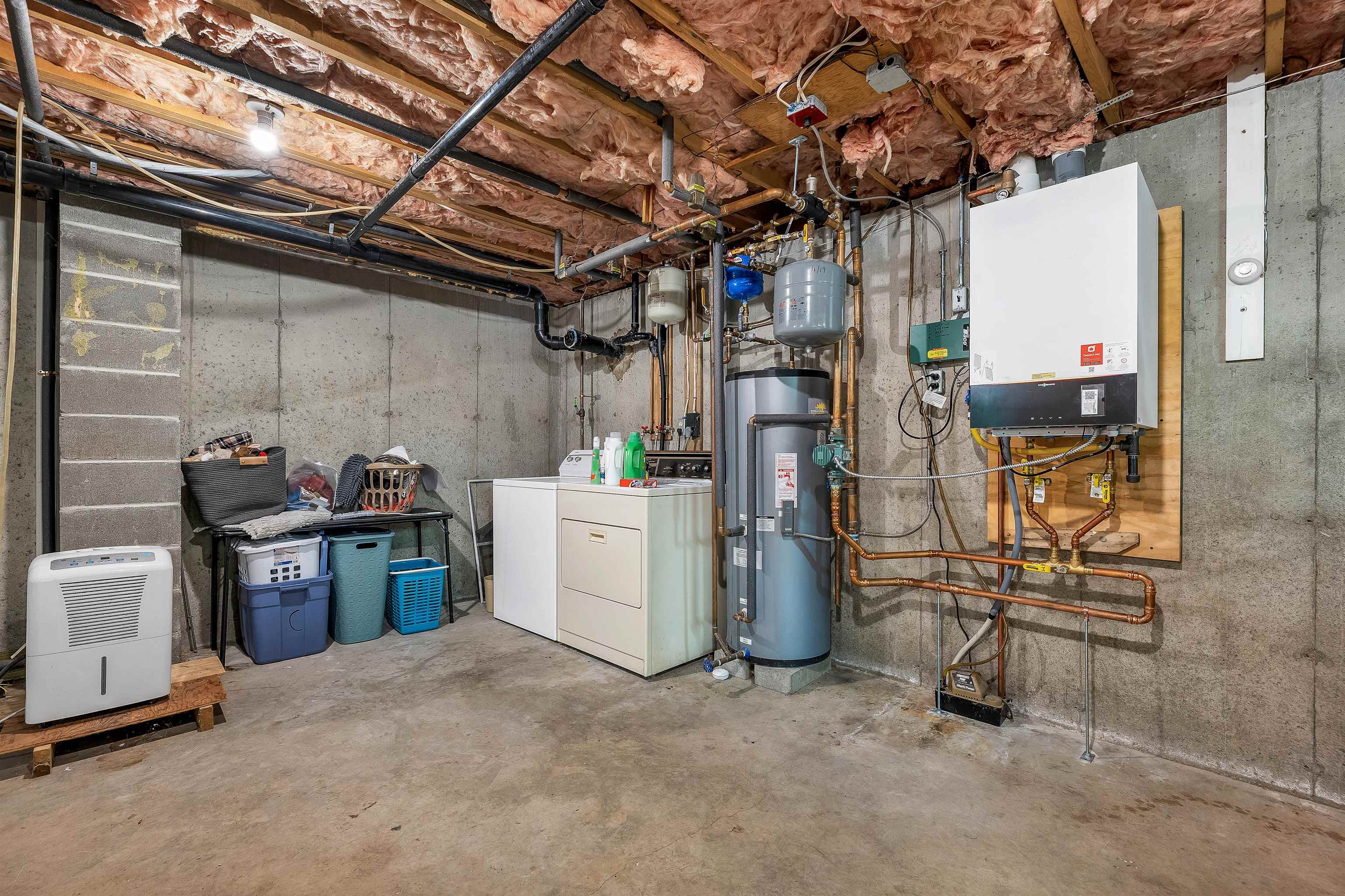 Basement utility room with laundry machines, hot water tanks, and exposed plumbing.