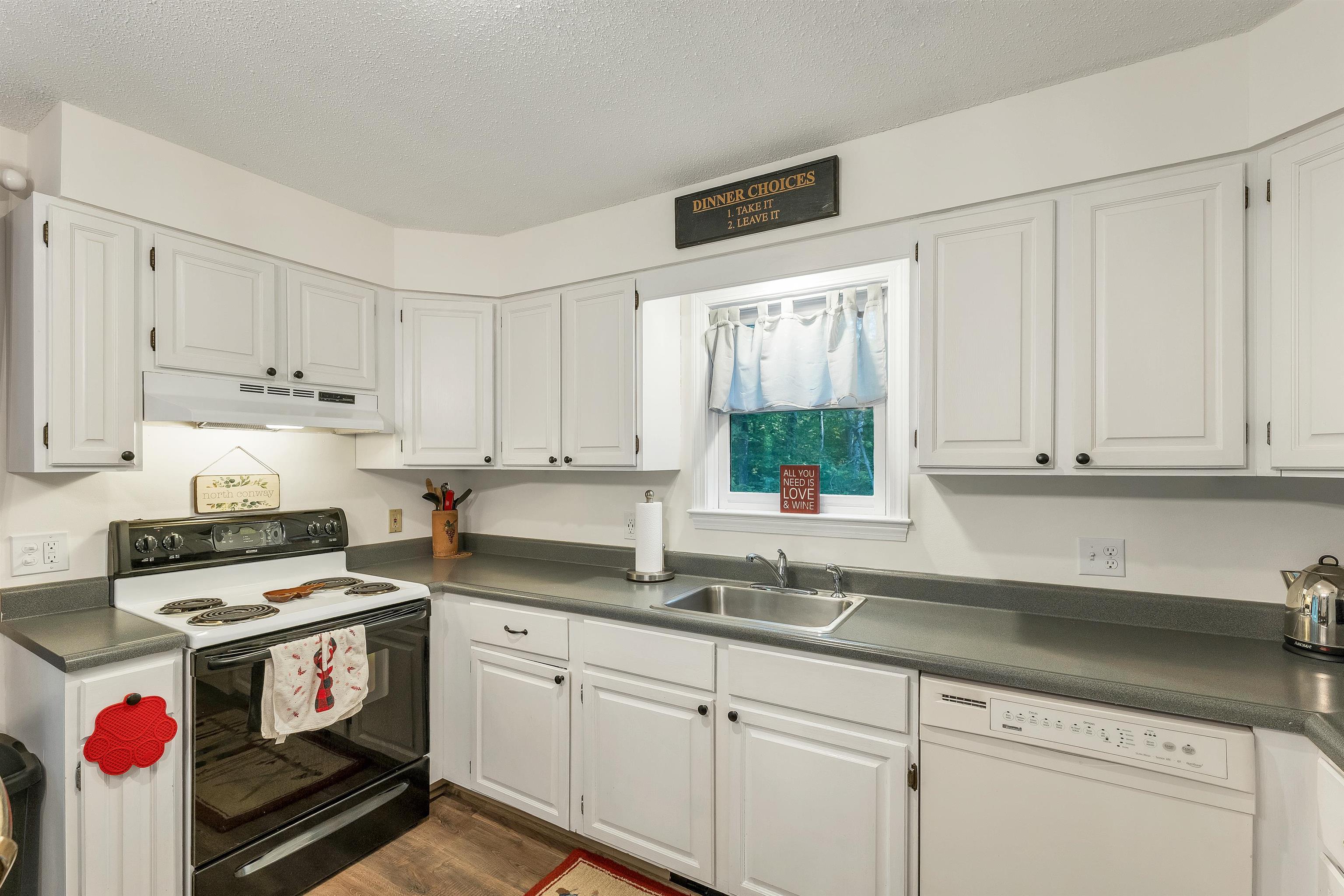 Kitchen with white cabinets, gray countertops, and a sink beneath a window overlooking trees.