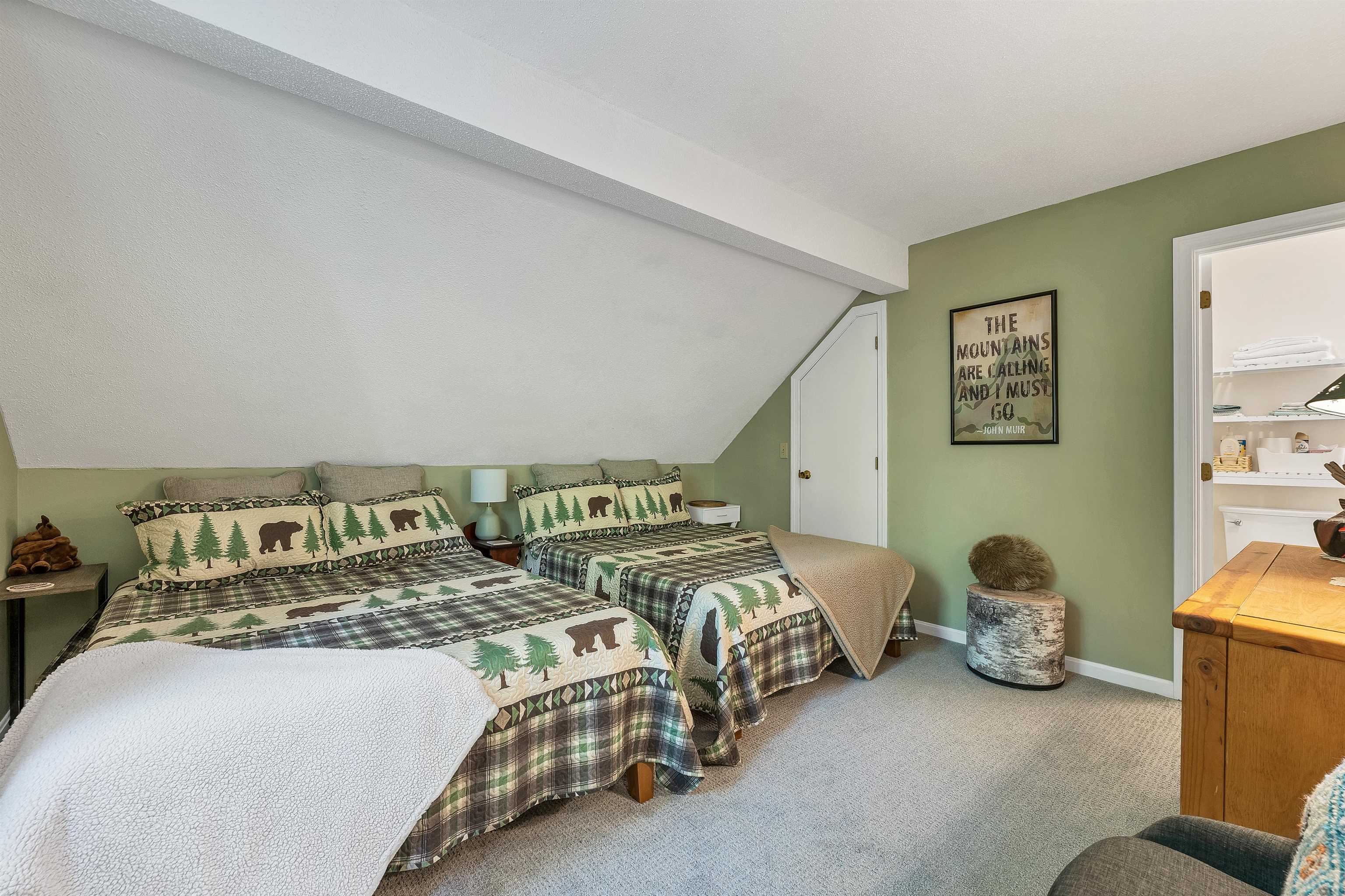 Bedroom with two woodland-patterned beds beneath a sloped ceiling and an adjoining bathroom.