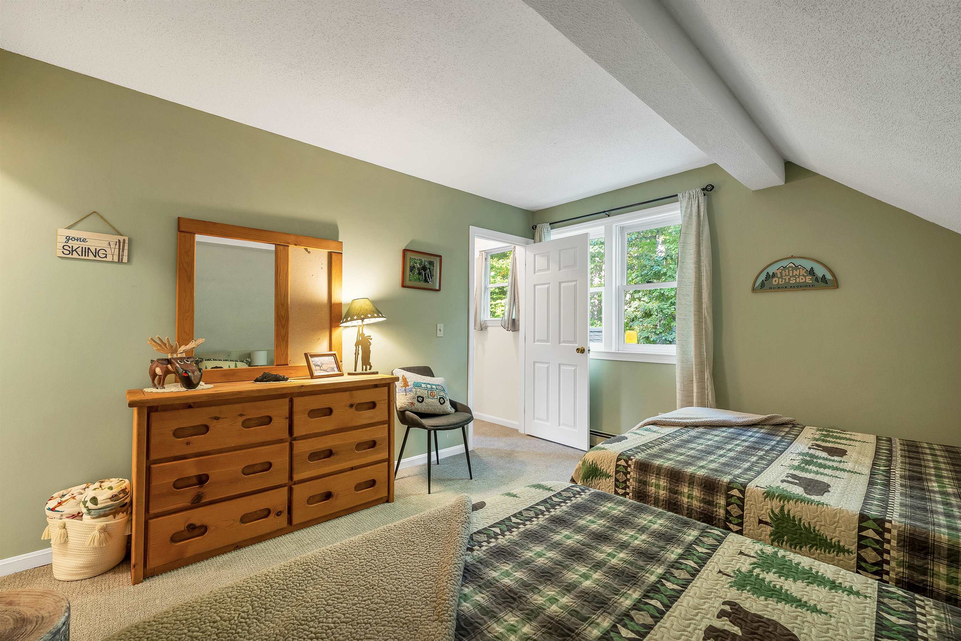 Bedroom with twin beds in green patchwork quilts, a wooden dresser, and a sloped ceiling.