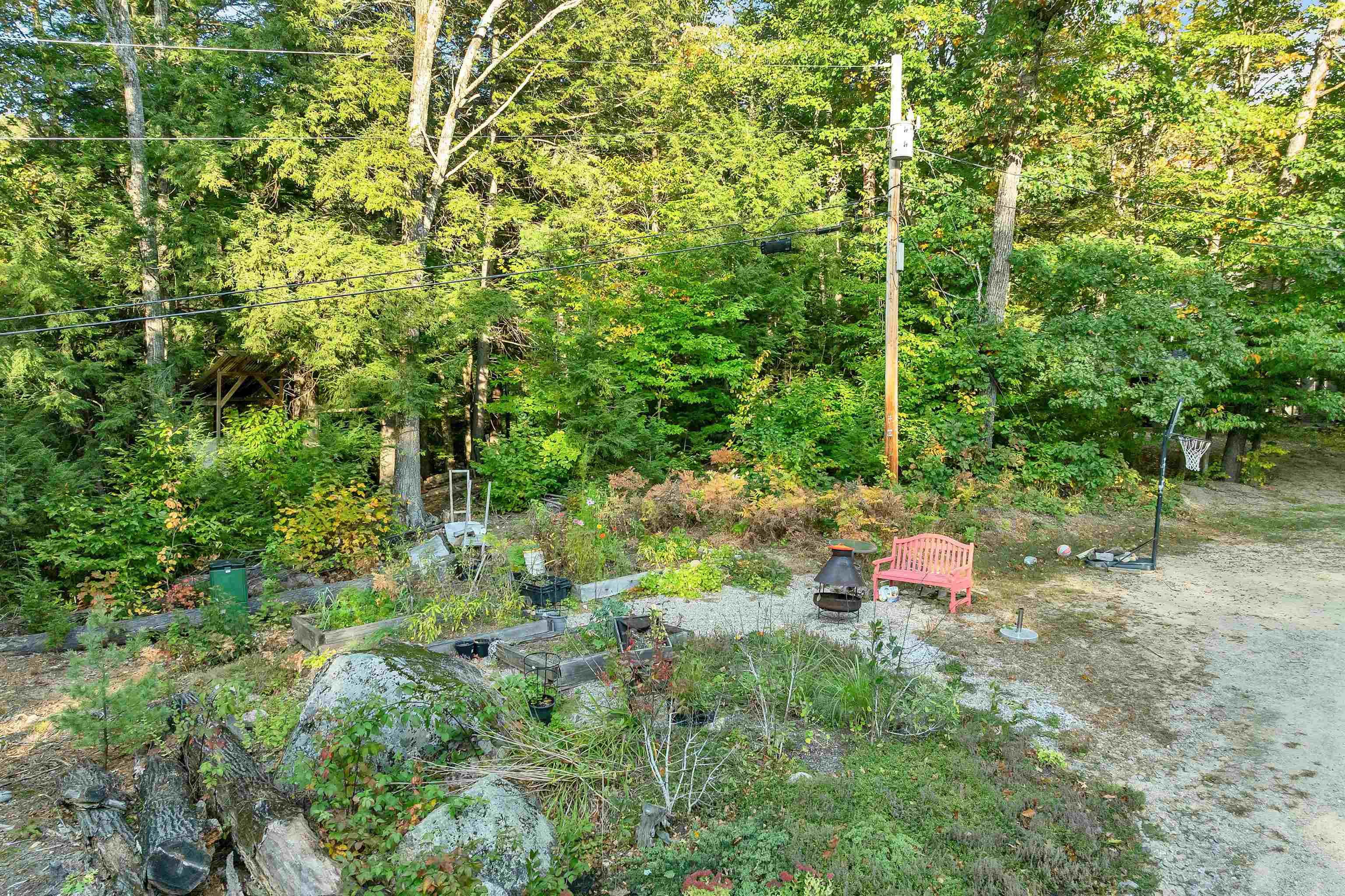 Wooded backyard with raised garden beds, a pink bench, chiminea, and basketball hoop.