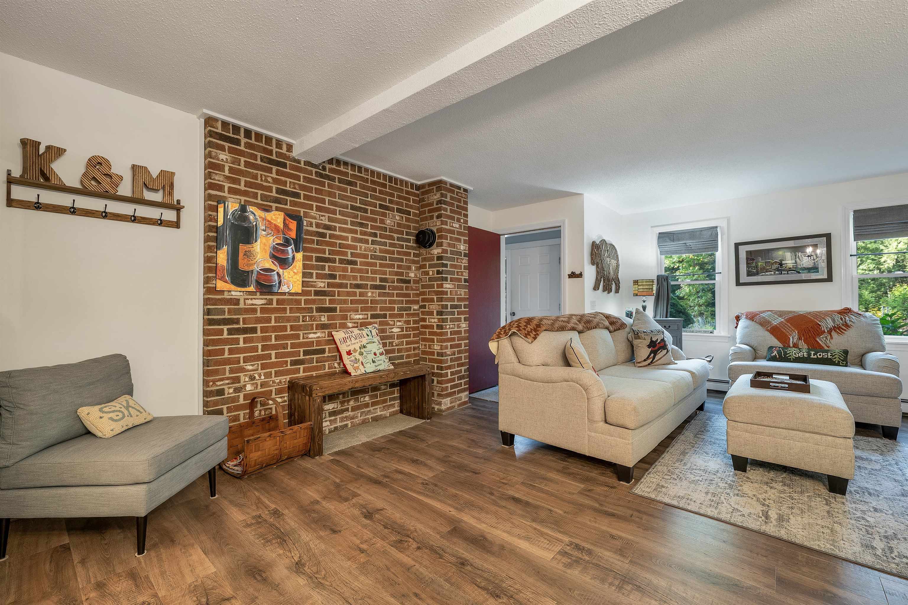Living room with an exposed brick accent wall, beige seating, and wood-look flooring.