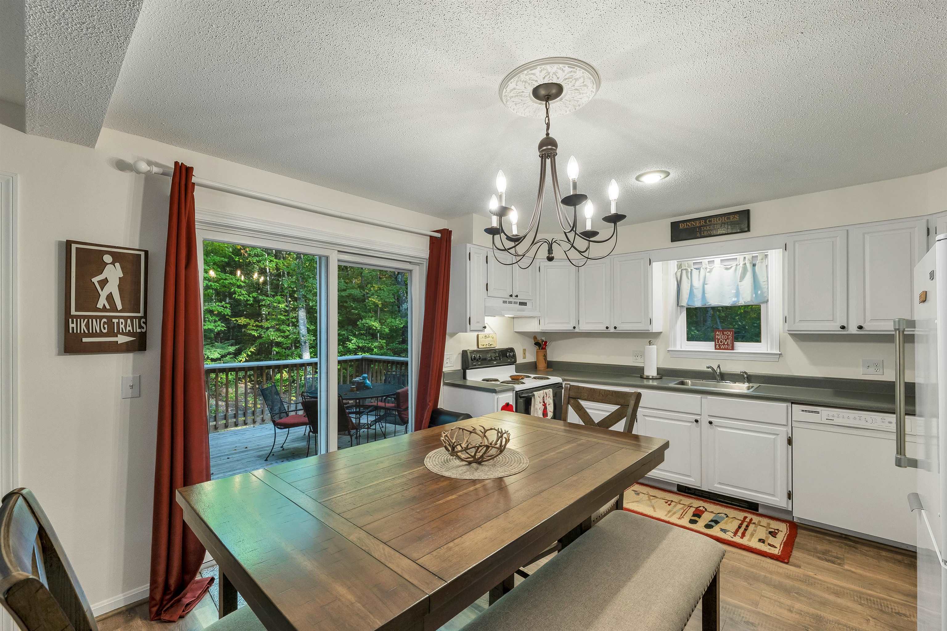Kitchen and dining area with white cabinets, a large wooden table, and sliding doors to a wooded deck.