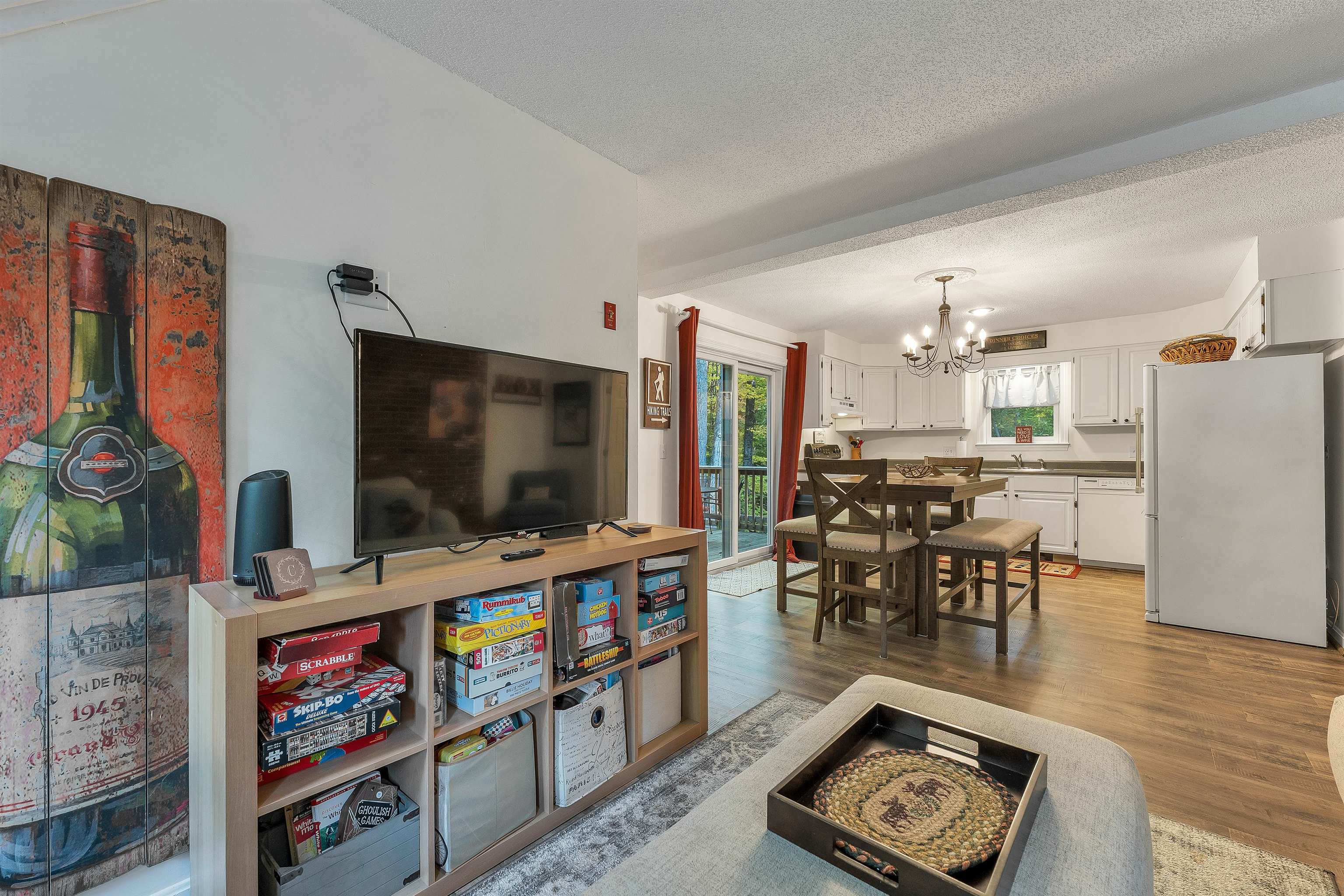 Open-plan living room and kitchen with board-game shelves, dining table, and white cabinetry.