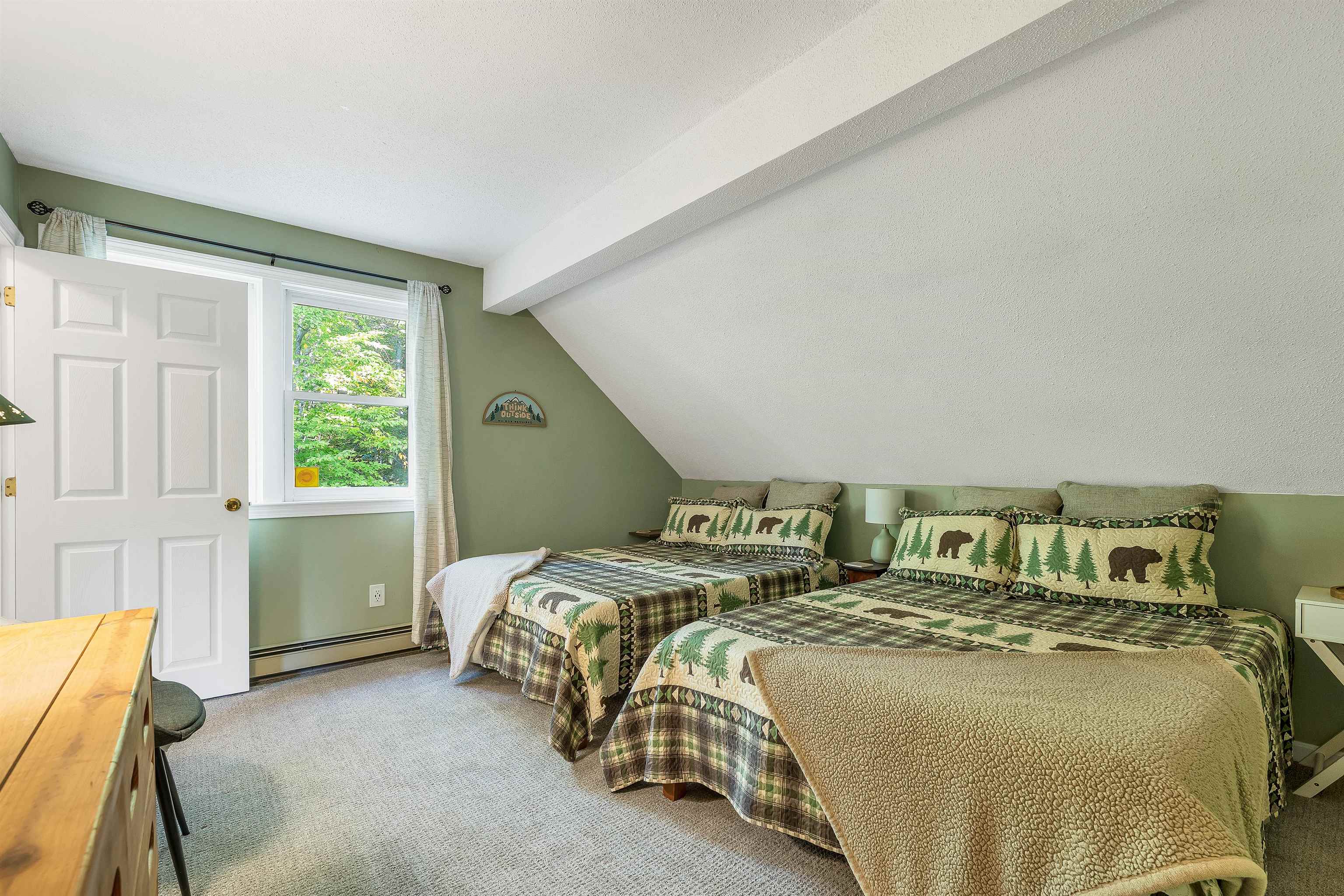 Bedroom with two bear-and-pine-tree patterned beds beneath a sloped ceiling.