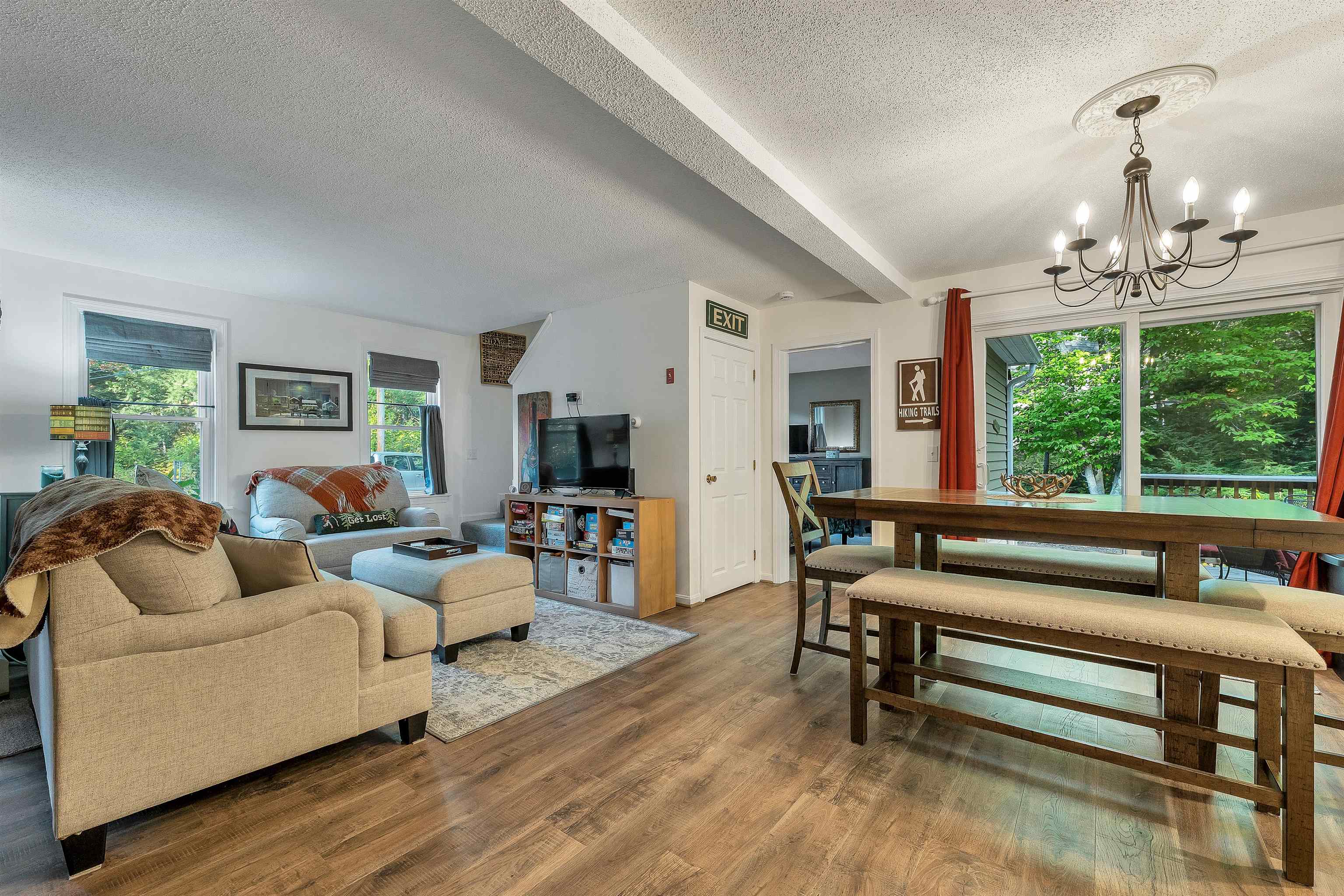Open-plan living and dining room with beige seating, a wooden table, and leafy views through large windows.