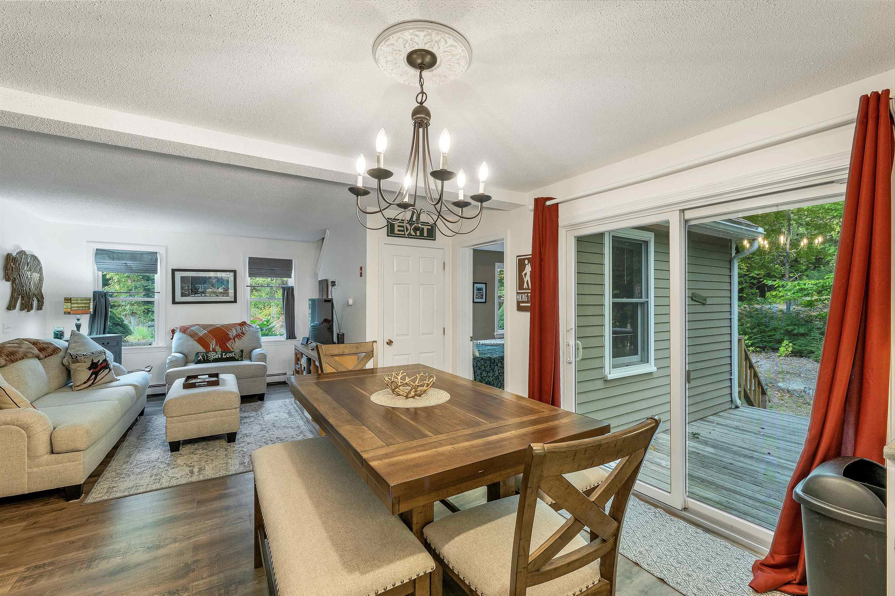Open living and dining area with a wooden table, chandelier, and sliding doors to a wooded deck.