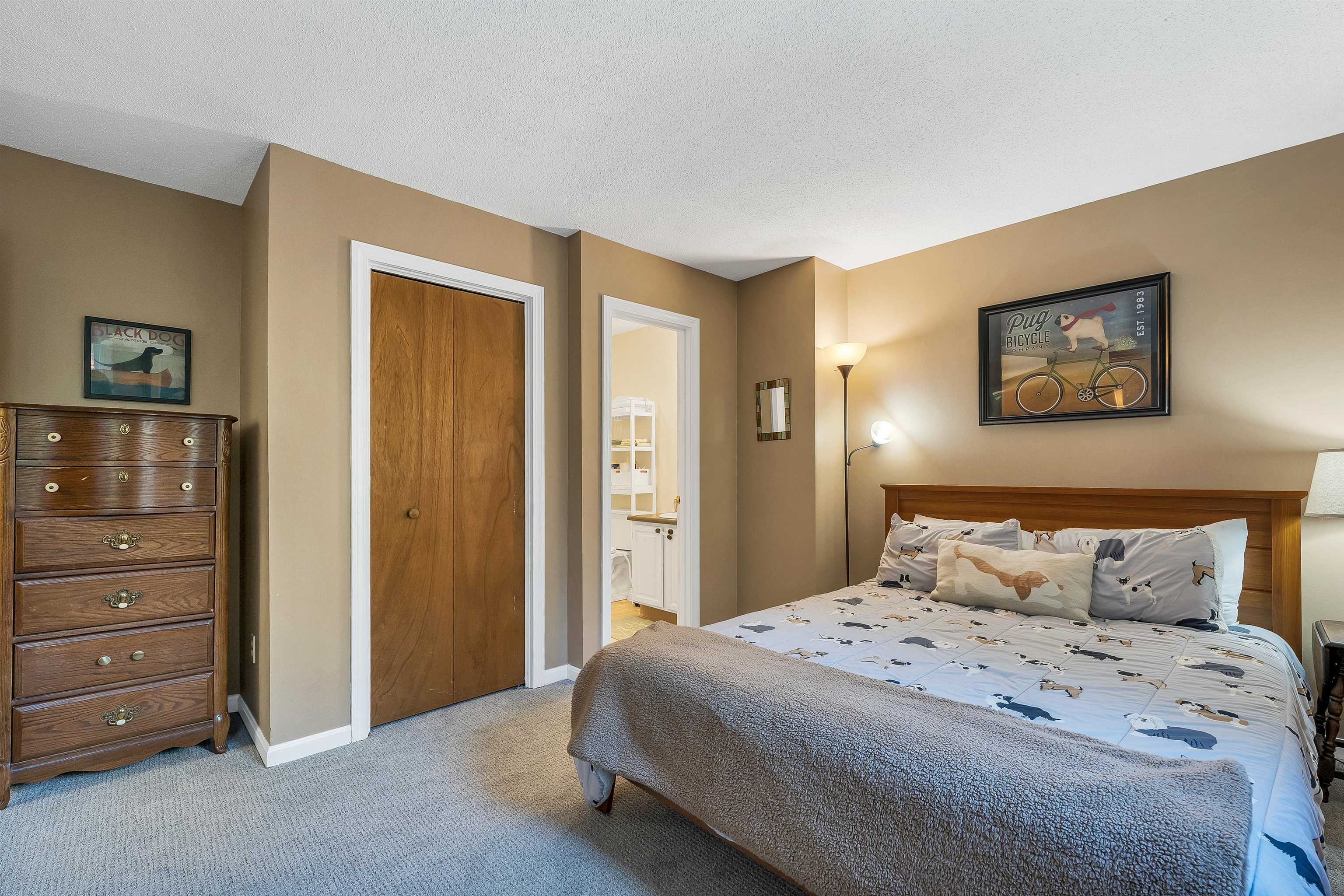 Bedroom with dog-print bedding, a wooden bed and dresser, and a doorway to an adjoining room.