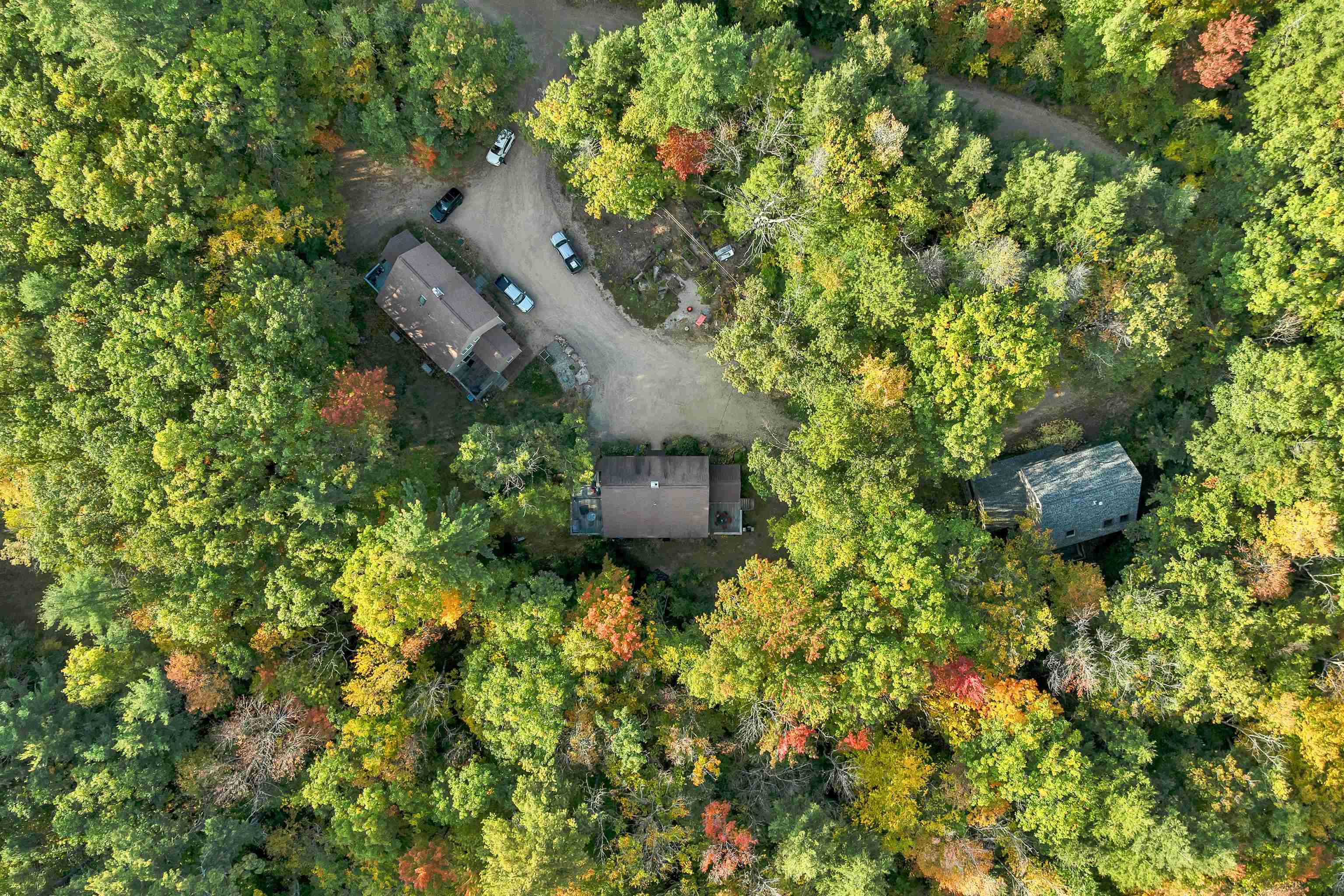 Aerial view of buildings and a gravel driveway amid autumn foliage.