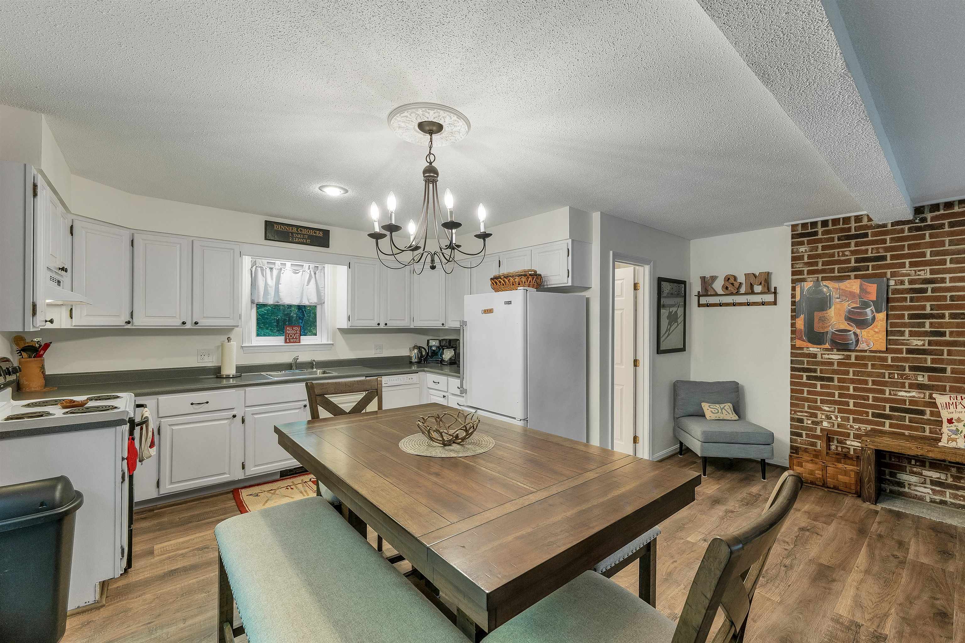 Kitchen and dining area with white cabinets, a large wooden table, and a brick accent wall.