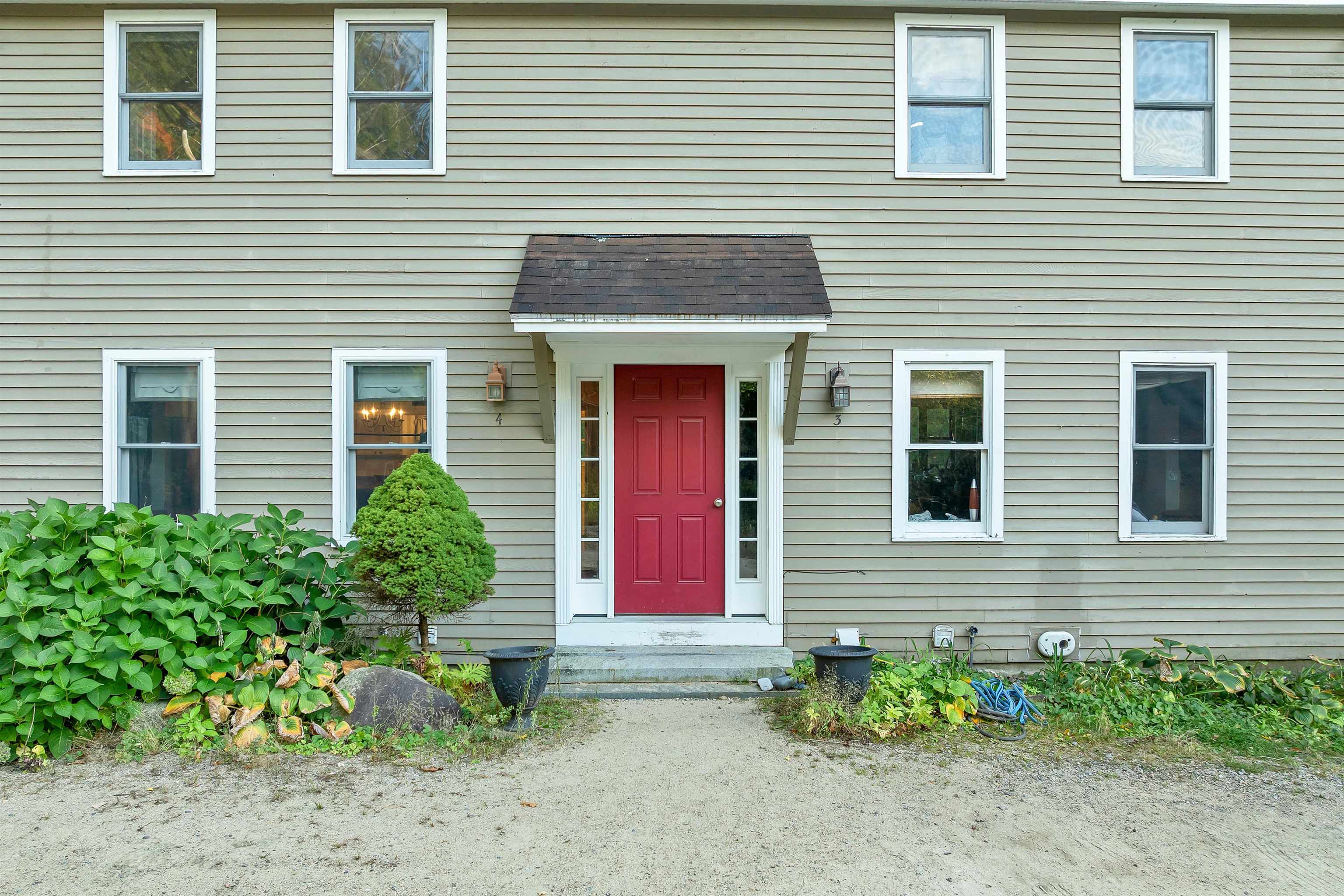 Two-story gray-sided home with a red front door, white-trimmed windows, and landscaped entry.