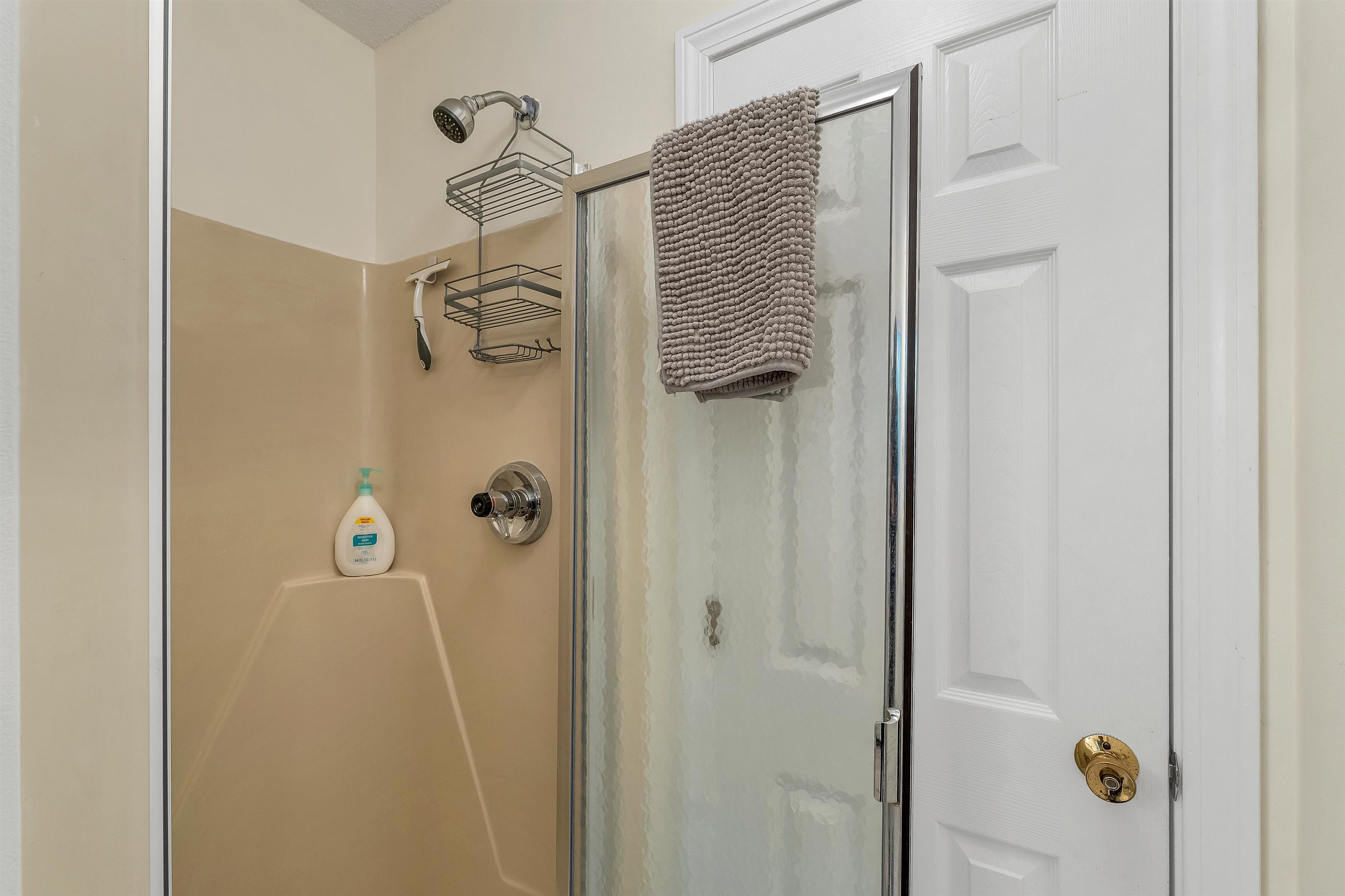Bathroom shower with beige surround, chrome fixtures, frosted glass door, and a gray towel.