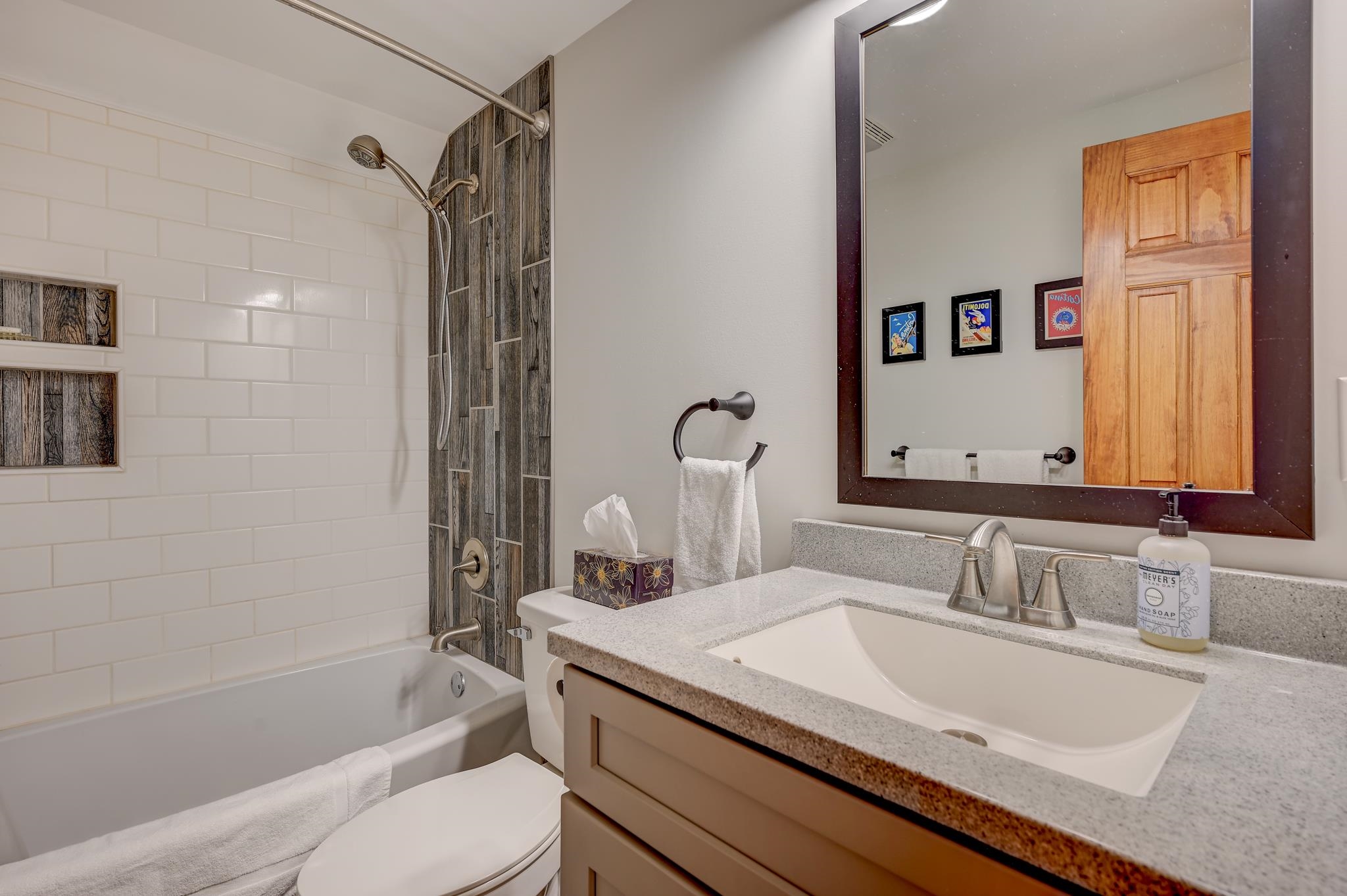 Bathroom with a white subway-tile tub surround, wood-look shower accents, and a speckled vanity countertop.