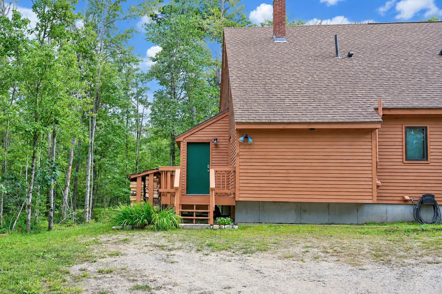 Wood-sided residence with a green entry door and small porch beside leafy trees.